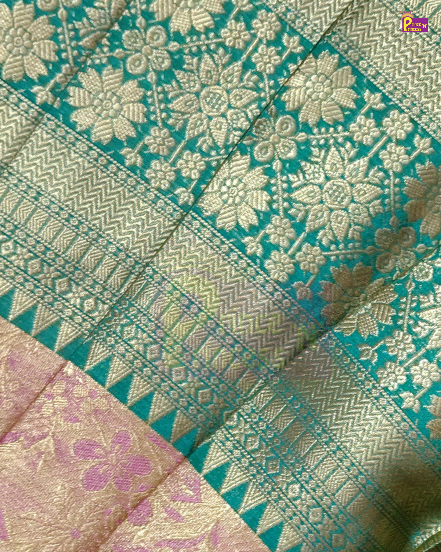A close-up of a teal and gold Banarasi silk saree fabric, showcasing intricate floral zari embroidery, geometric borders, and a pink and gold pallu section.