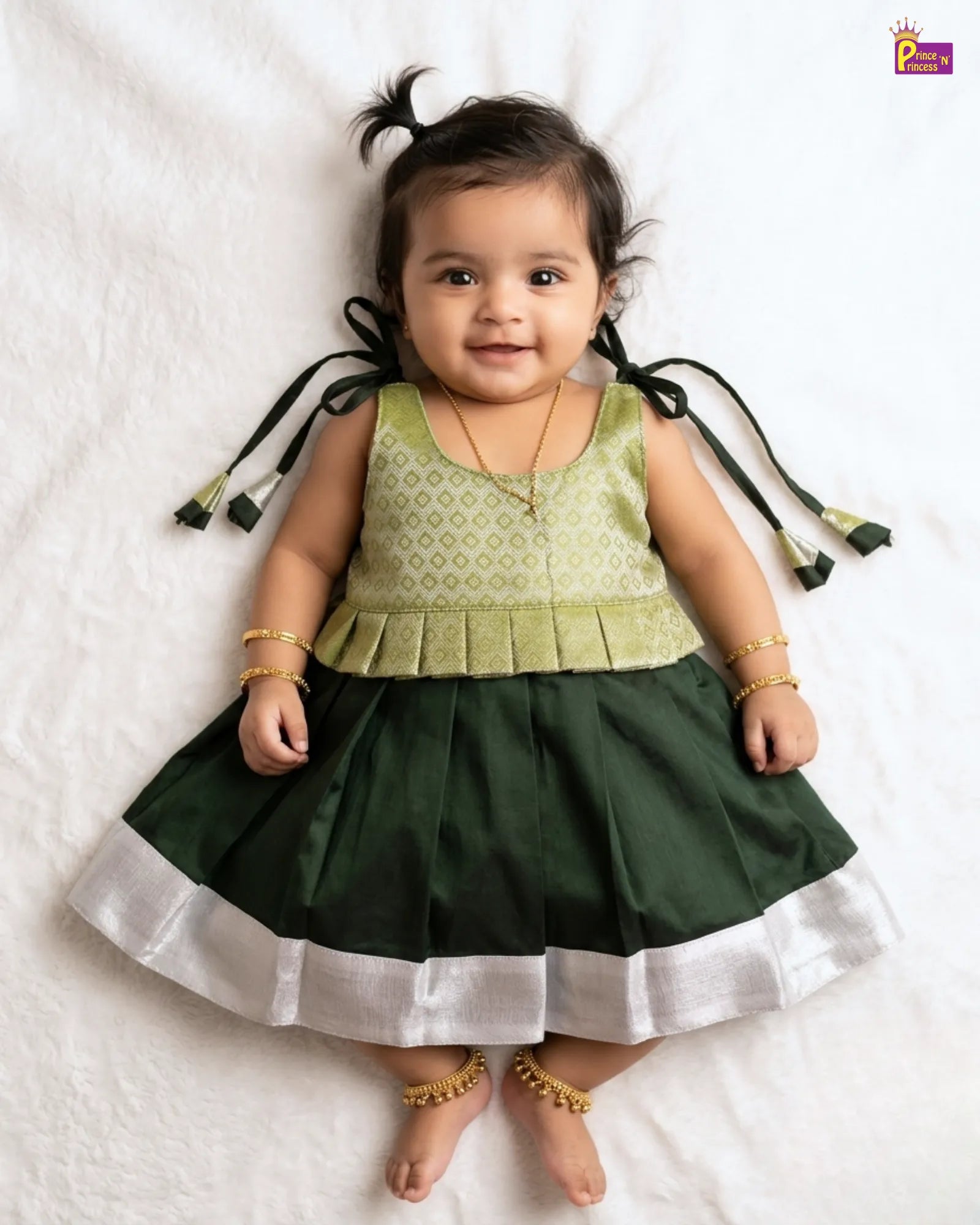 Baby wearing a green and dark green dress with decorative elements on a white background