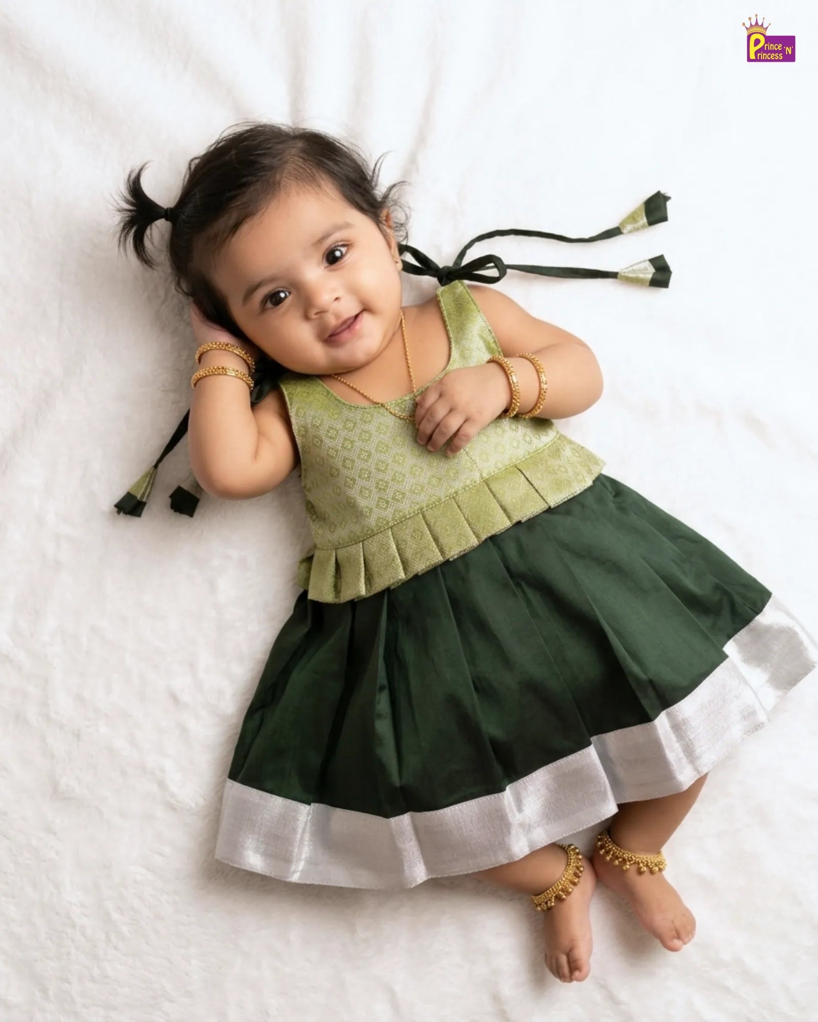 Baby wearing a green and dark green dress with white trim on a white background