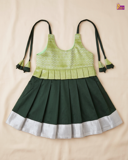 A sleeveless children's dress laid flat on a light beige fabric background. The dress has a light green patterned bodice, a darker green pleated skirt, and a contrasting light silver-white border at the bottom.