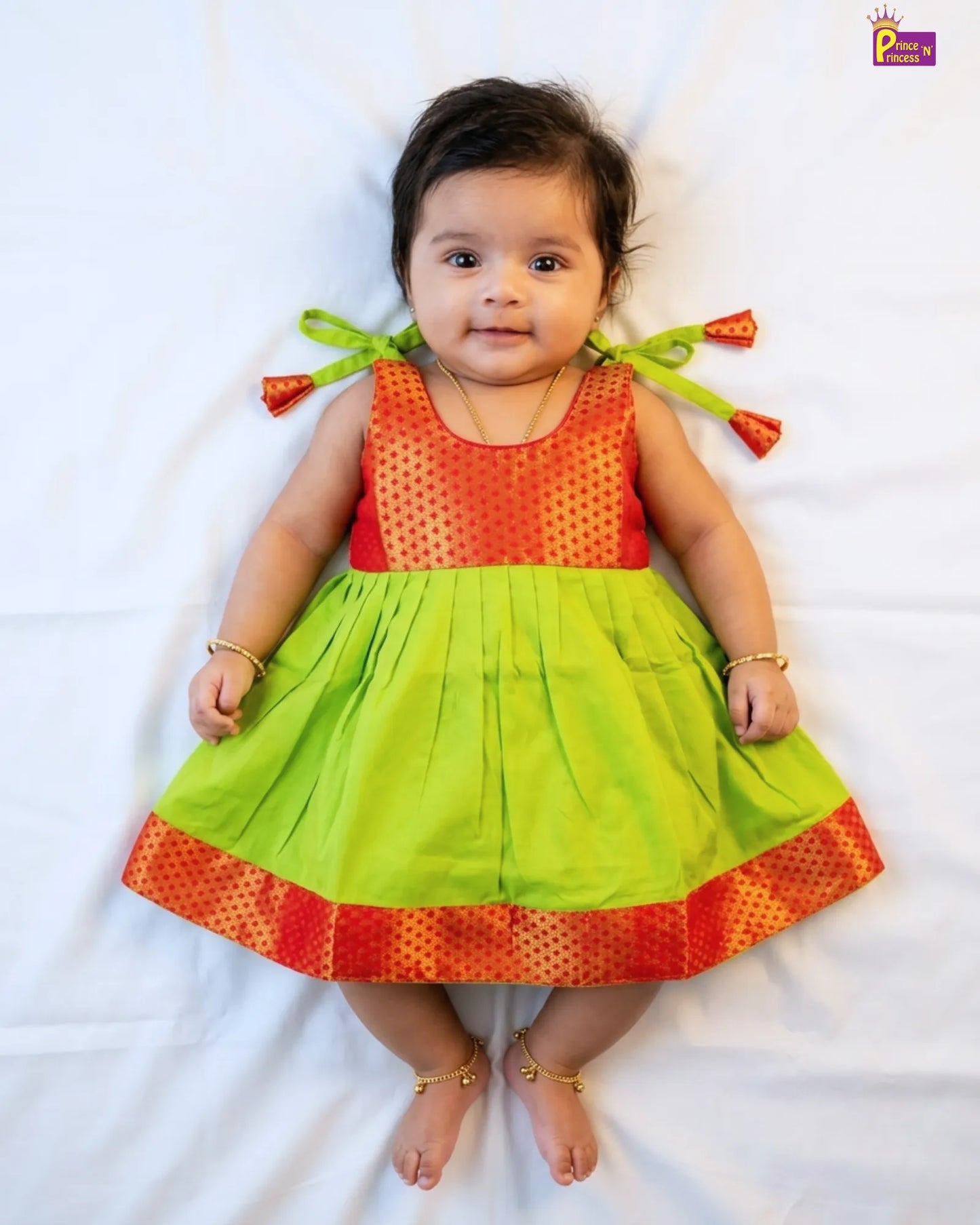 Baby wearing a colorful dress with orange top and green bottom on a white background