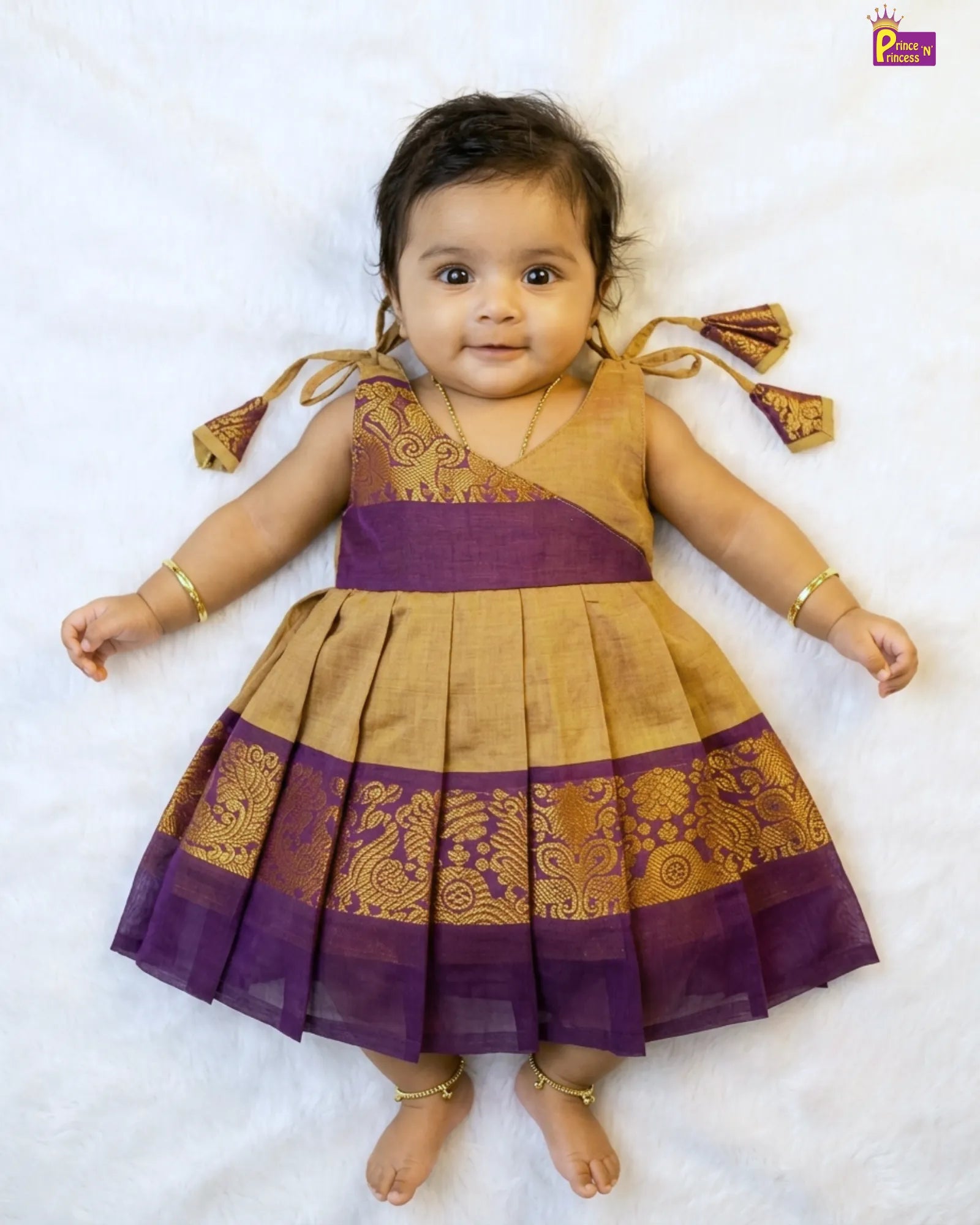 Baby wearing a traditional purple and gold dress on a white background