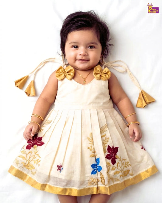Baby wearing a white dress with floral patterns and gold accents on a white background