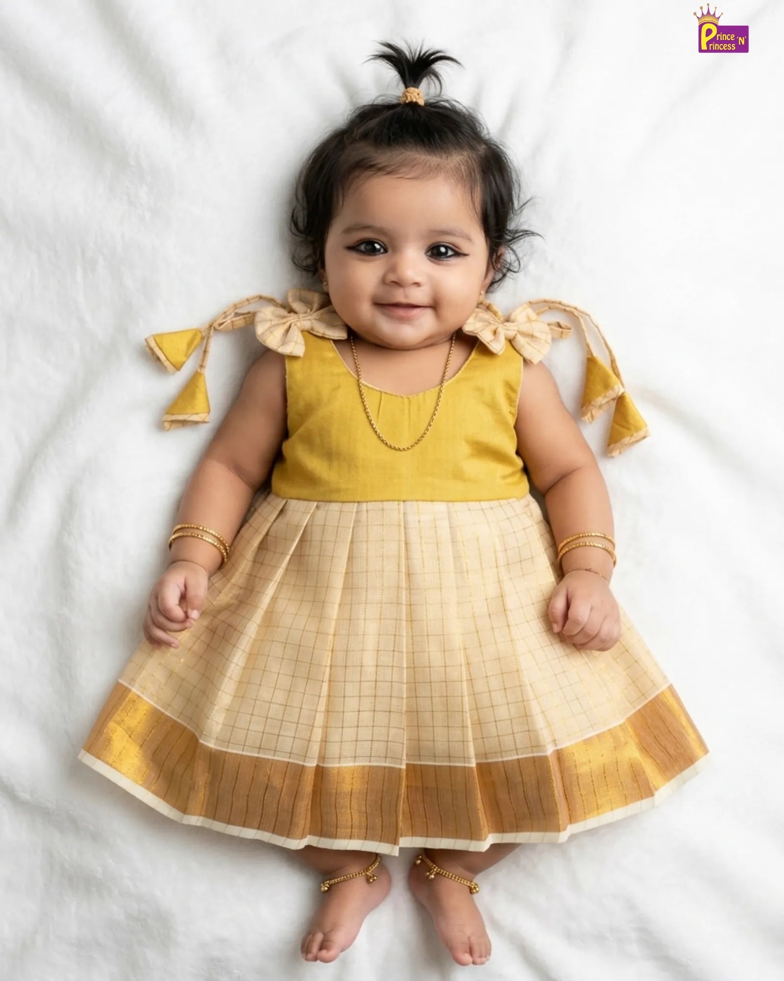 Baby wearing a yellow and beige traditional outfit on a white background