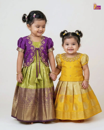 Two young girls modeling traditional Indian ethnic wear. The girl on the left wears a purple and olive green kurta set with a gold zari border, and the girl on the right wears a matching yellow kurta set with a gold zari border.