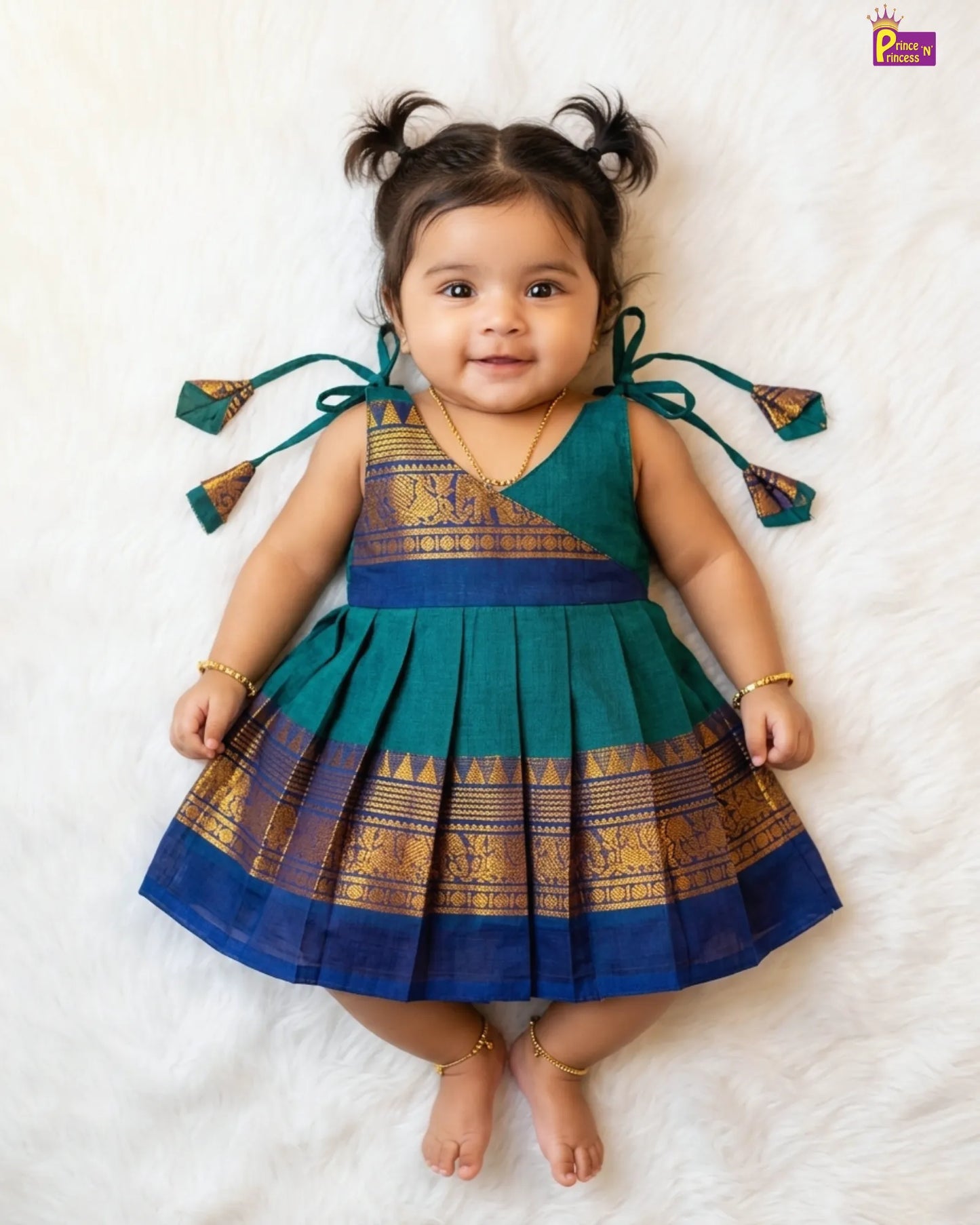 Baby wearing a traditional green and blue dress with decorative elements on a white background
