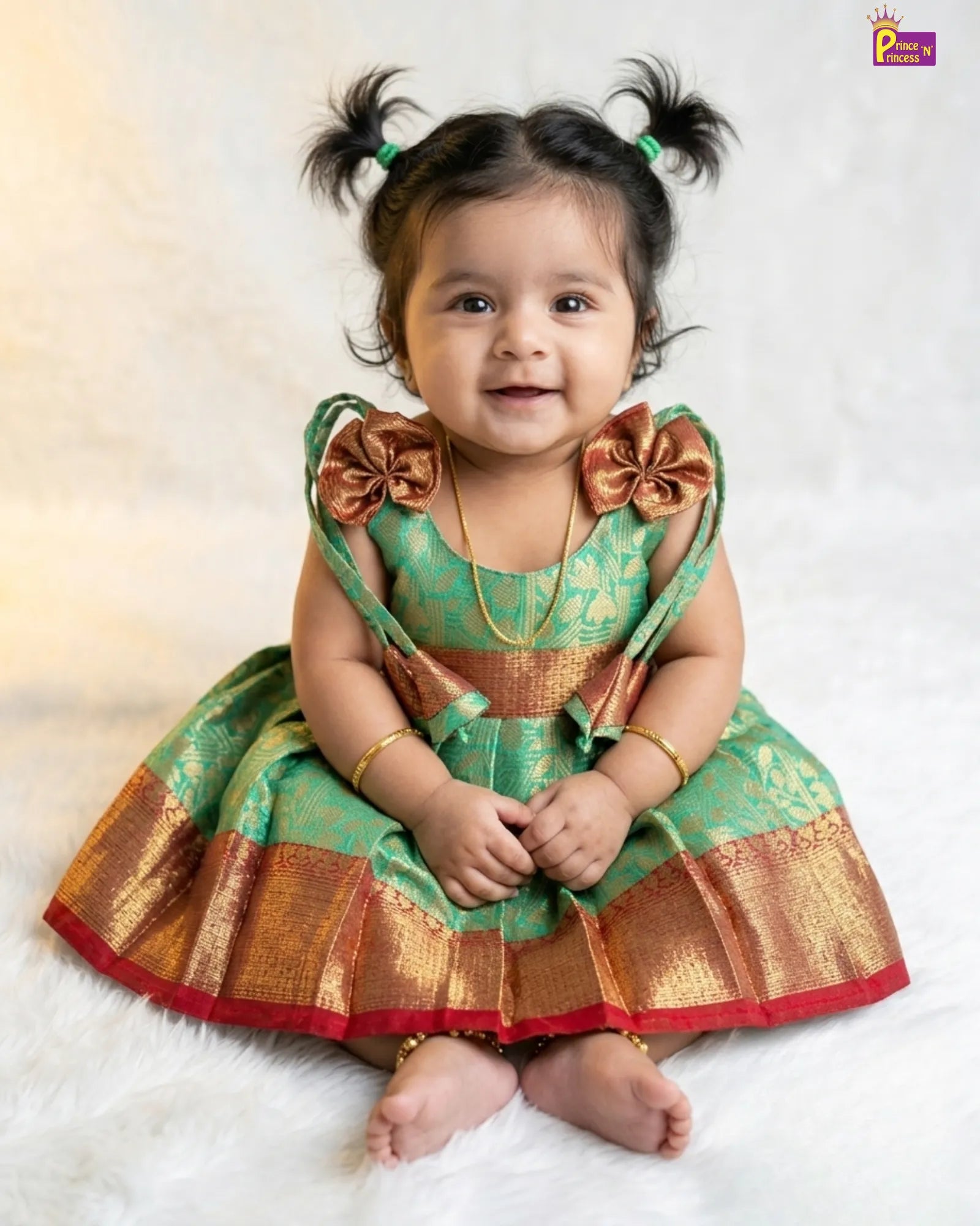 Baby in a green and gold traditional outfit with pigtails on a white background