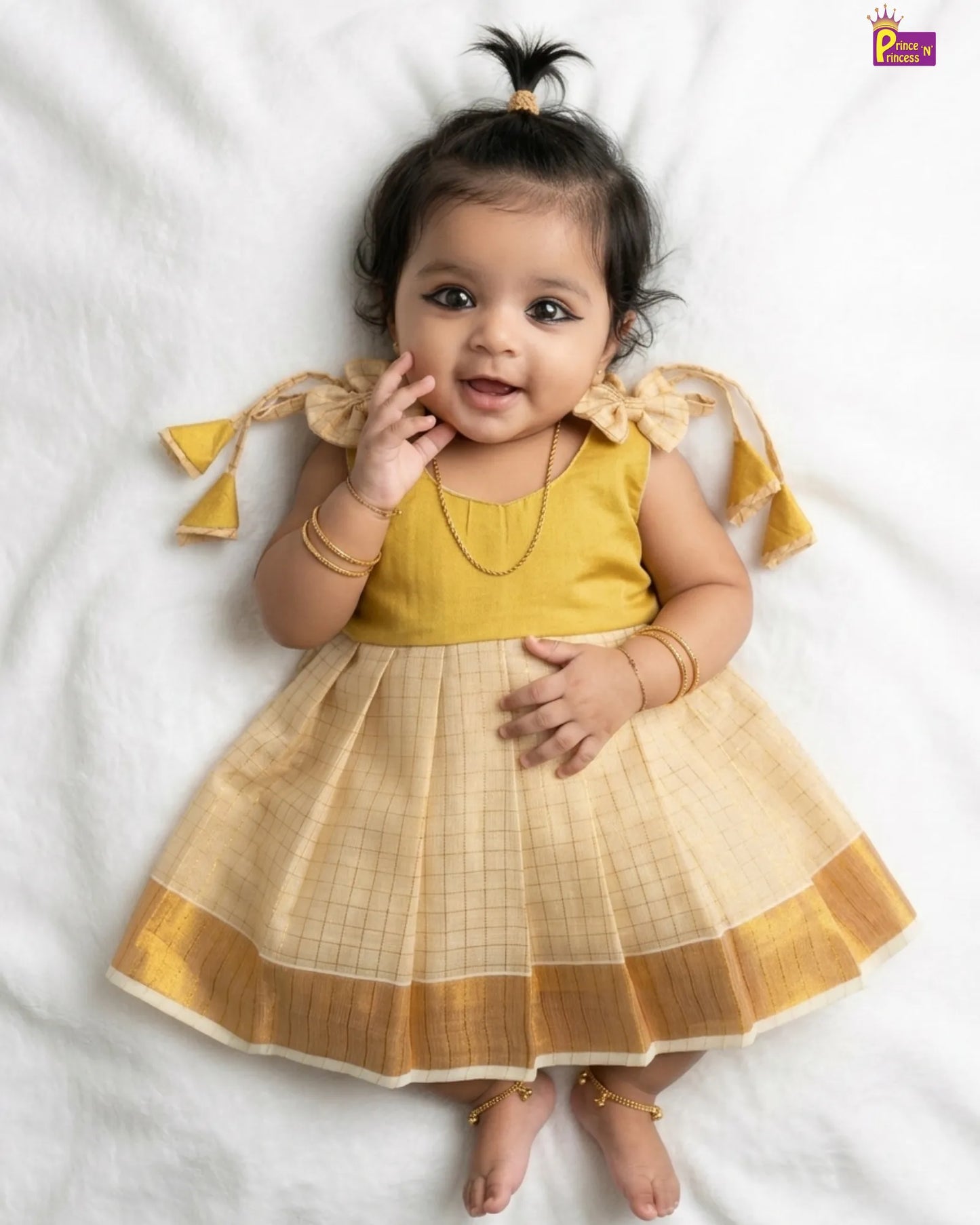 Baby wearing a yellow and gold traditional outfit on a white background