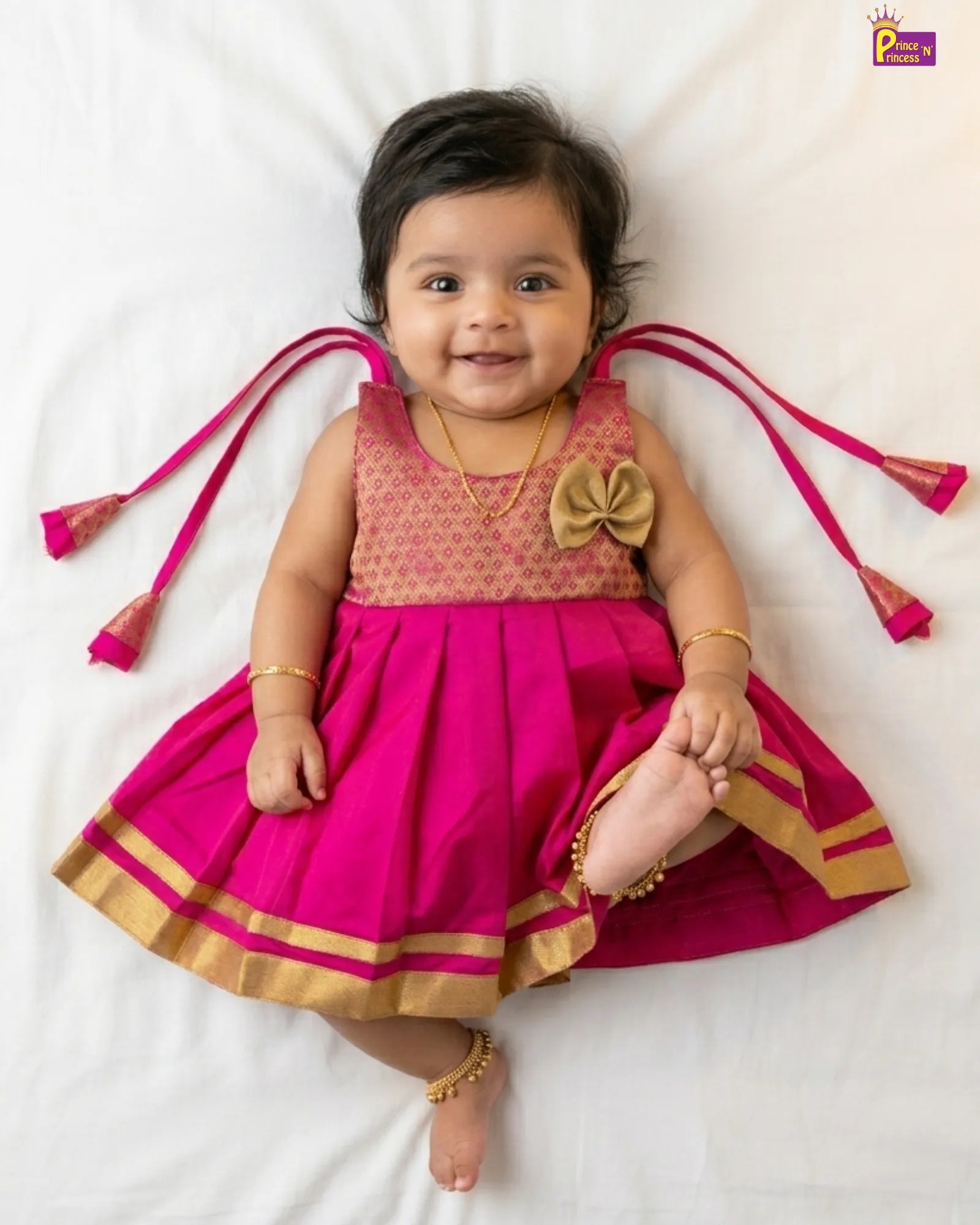 Baby wearing a pink and gold traditional outfit with decorative elements on a white background