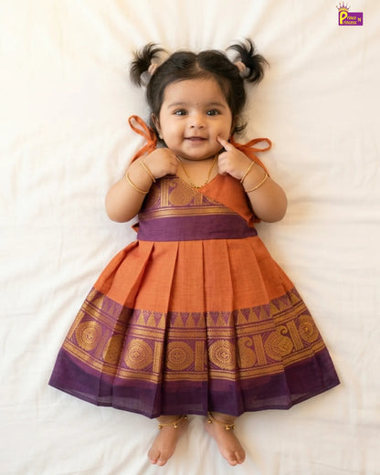 Baby wearing a traditional orange and purple dress on a white background