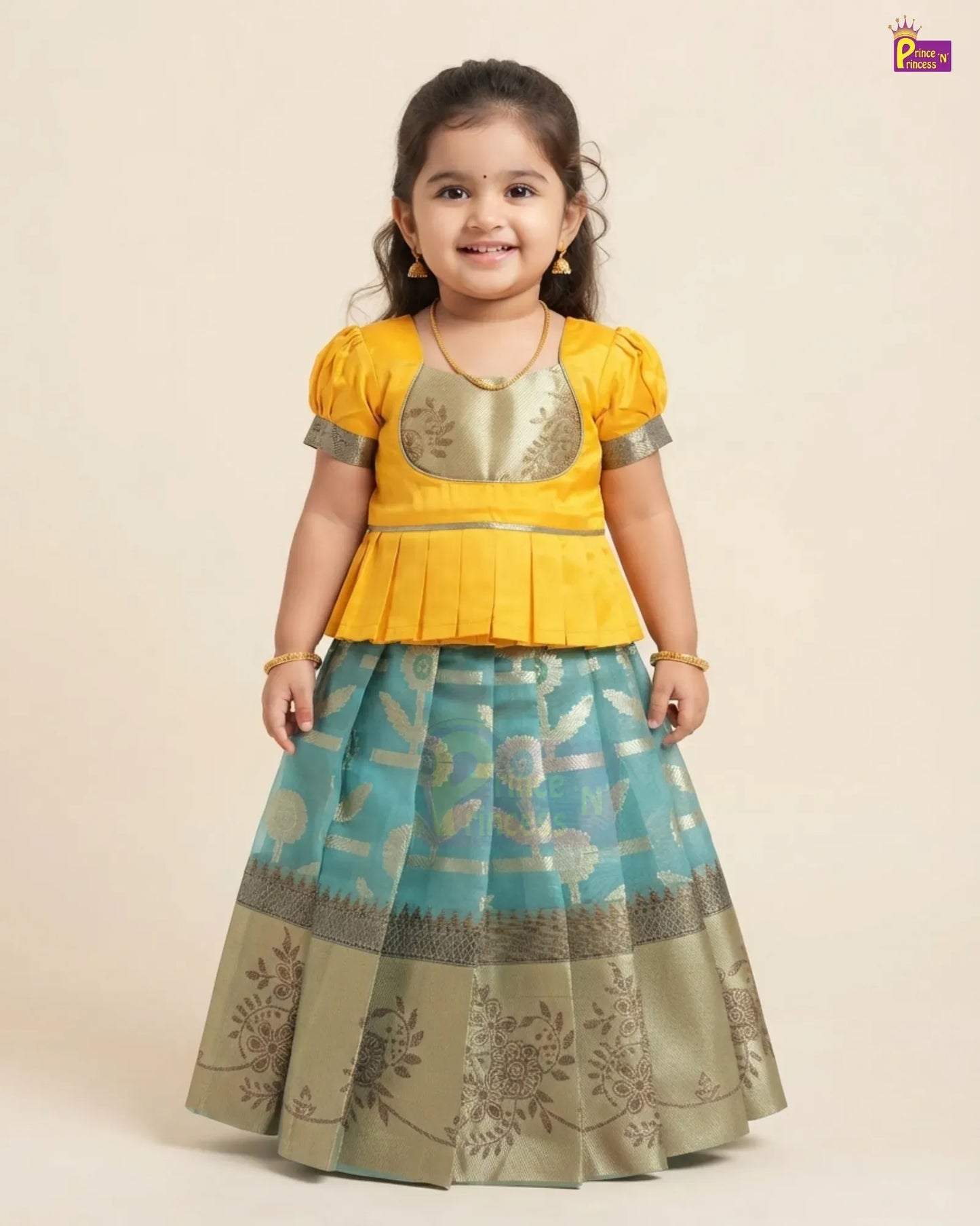 A young girl modeling a traditional Indian ethnic outfit consisting of a bright yellow peplum top with metallic gold embroidery and a matching pleated skirt in turquoise blue and beige with floral patterns.