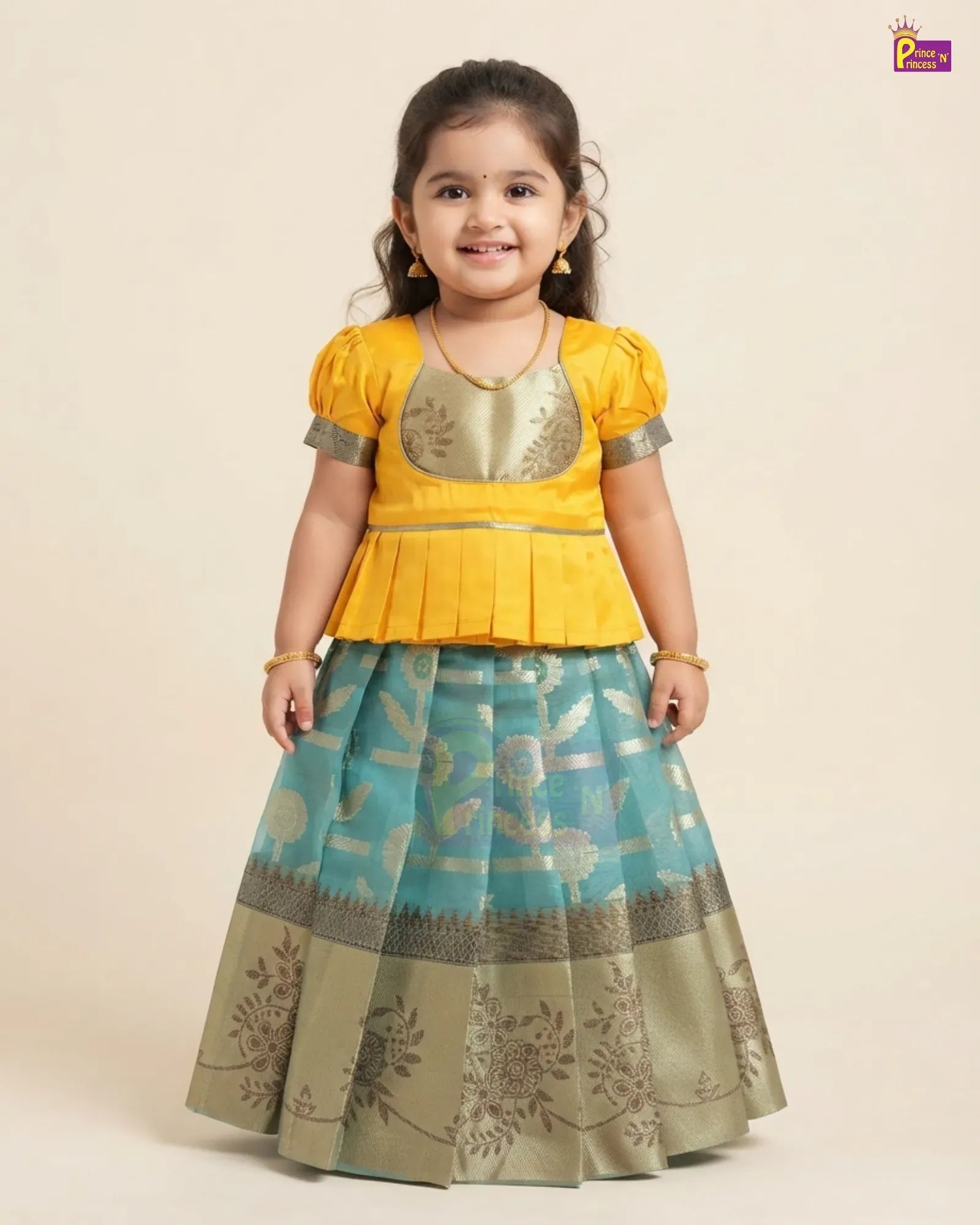A young girl modeling a traditional Indian ethnic outfit consisting of a bright yellow peplum top with metallic gold embroidery and a matching pleated skirt in turquoise blue and beige with floral patterns.