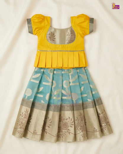 A traditional Indian girl's dress featuring a bright yellow peplum top with grey sleeve cuffs and a light blue pleated skirt with beige floral patterns and a metallic border, laid flat on a cream fabric background.