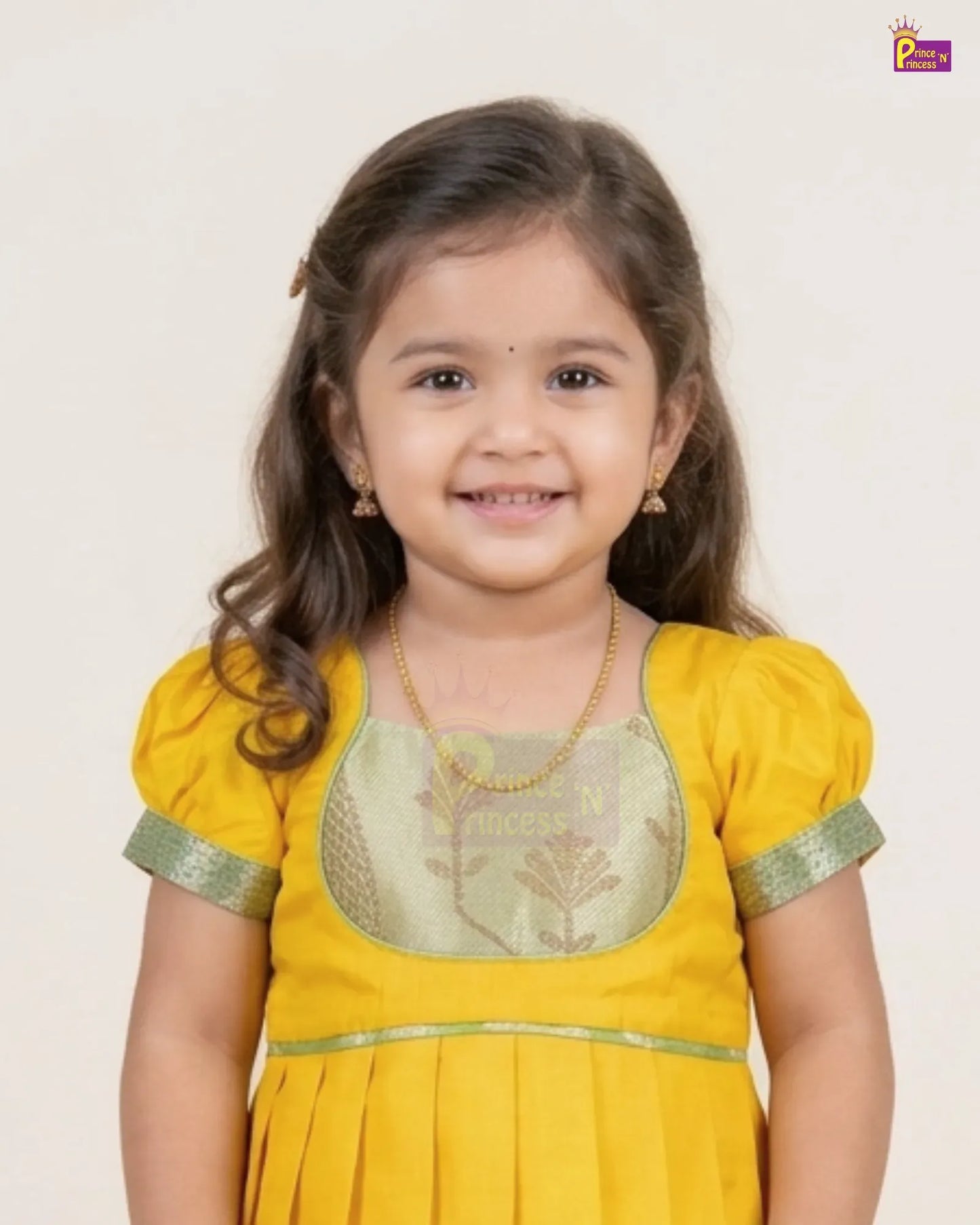 A young girl with long brown hair smiling, wearing a yellow traditional outfit with a light green embroidered chest panel and green trim on the sleeves, set against a plain off-white background.