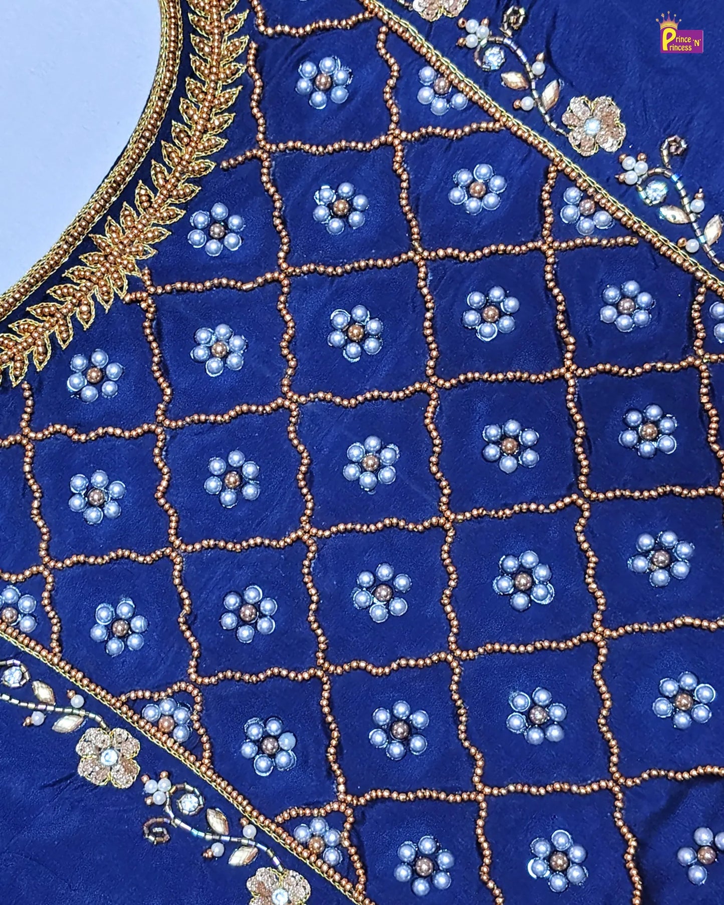 Close-up of blue fabric with intricate gold and white embroidery on a light blue background