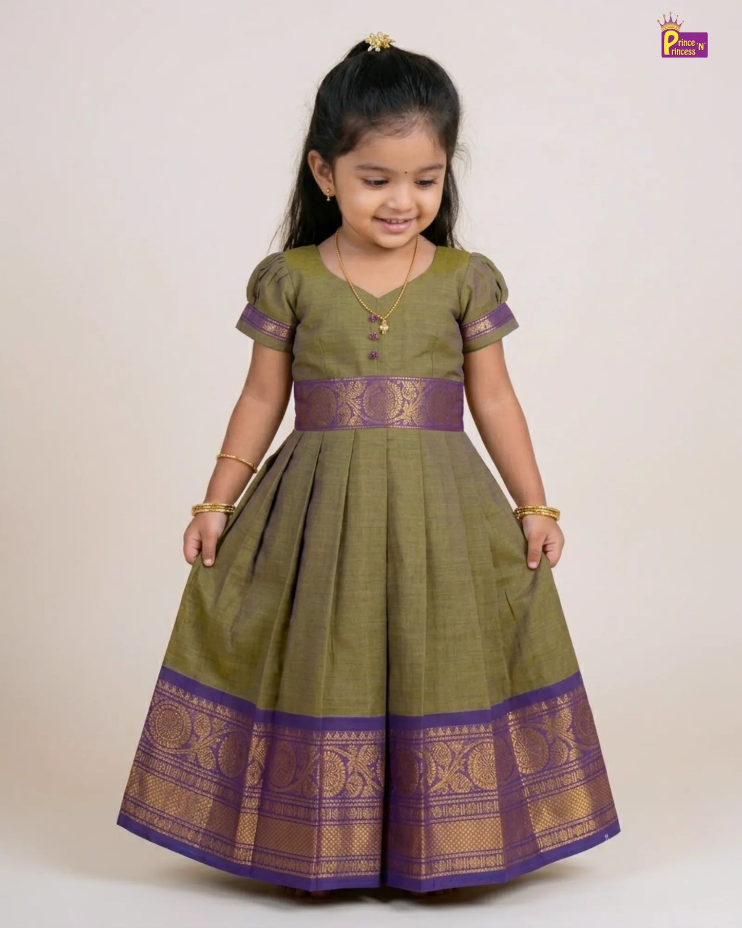 Young girl wearing a green and purple traditional dress on a plain background