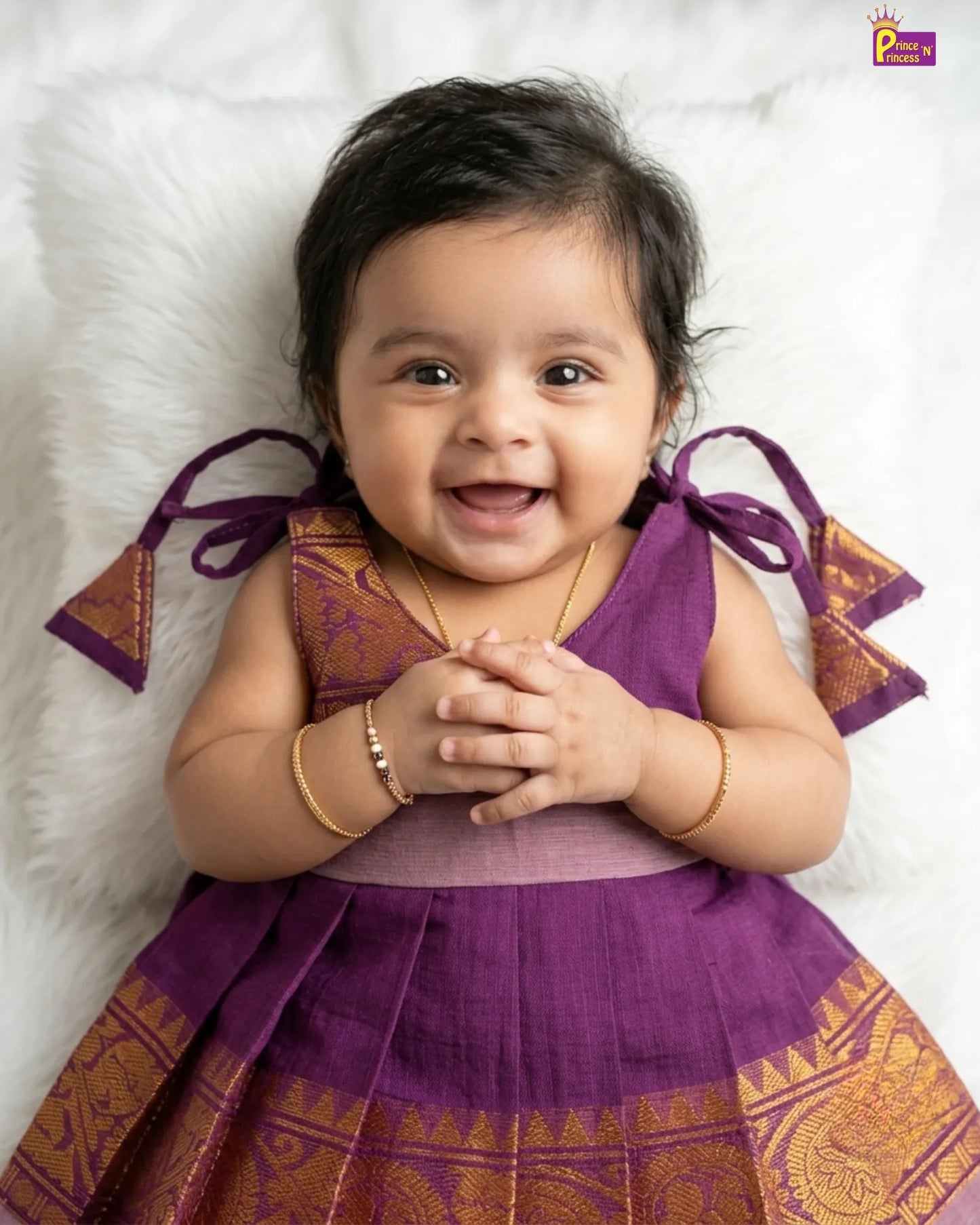 Baby in a purple traditional outfit with gold patterns on a white background
