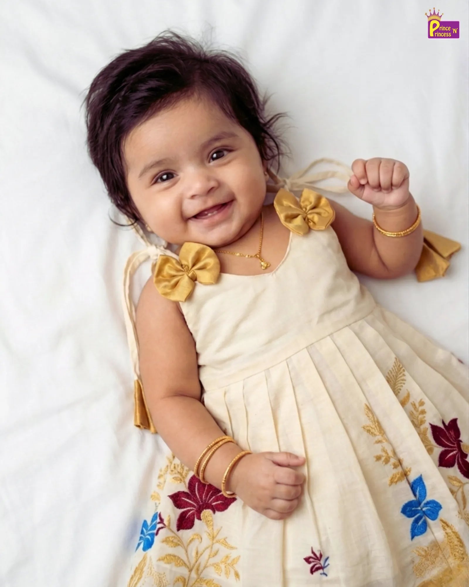 Baby in a cream-colored dress with floral patterns lying on a white surface