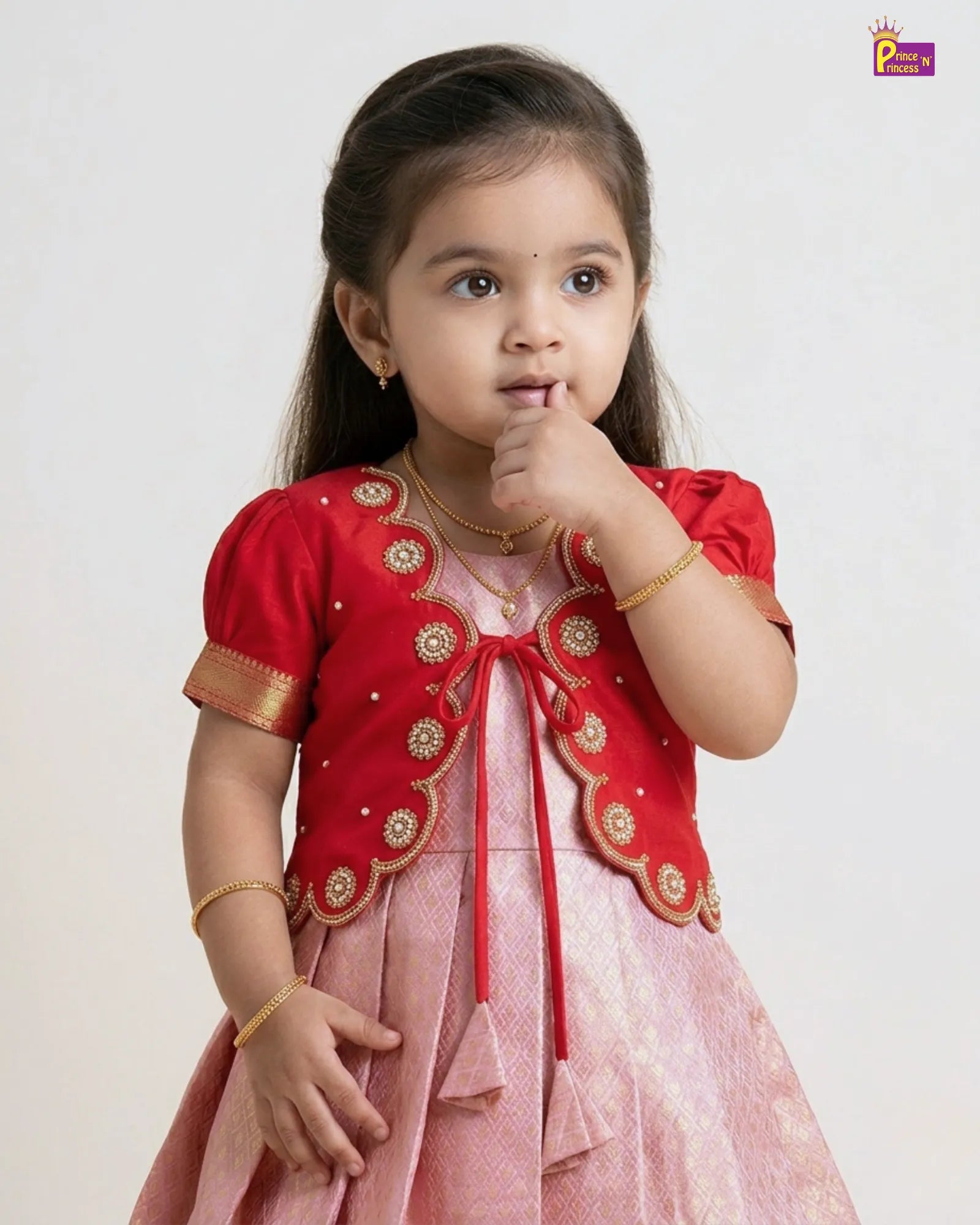 Young girl in a red and pink traditional outfit with gold accents on a white background