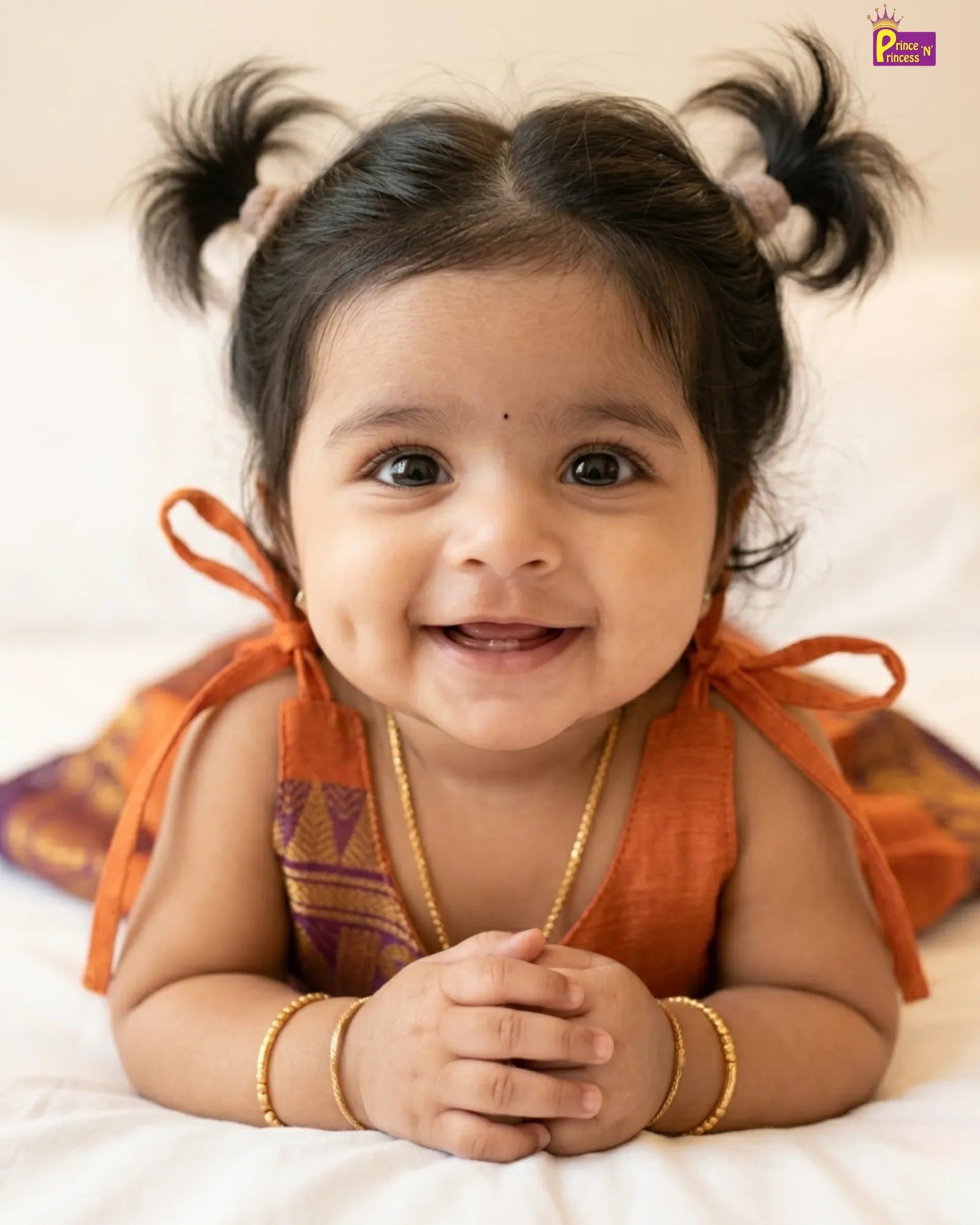 Smiling baby with pigtails wearing an orange traditional outfit on a white background