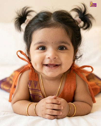 Smiling baby with pigtails wearing an orange traditional outfit on a white background