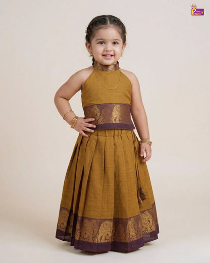 Young girl wearing a traditional mustard yellow and purple dress with intricate patterns on a white background.
