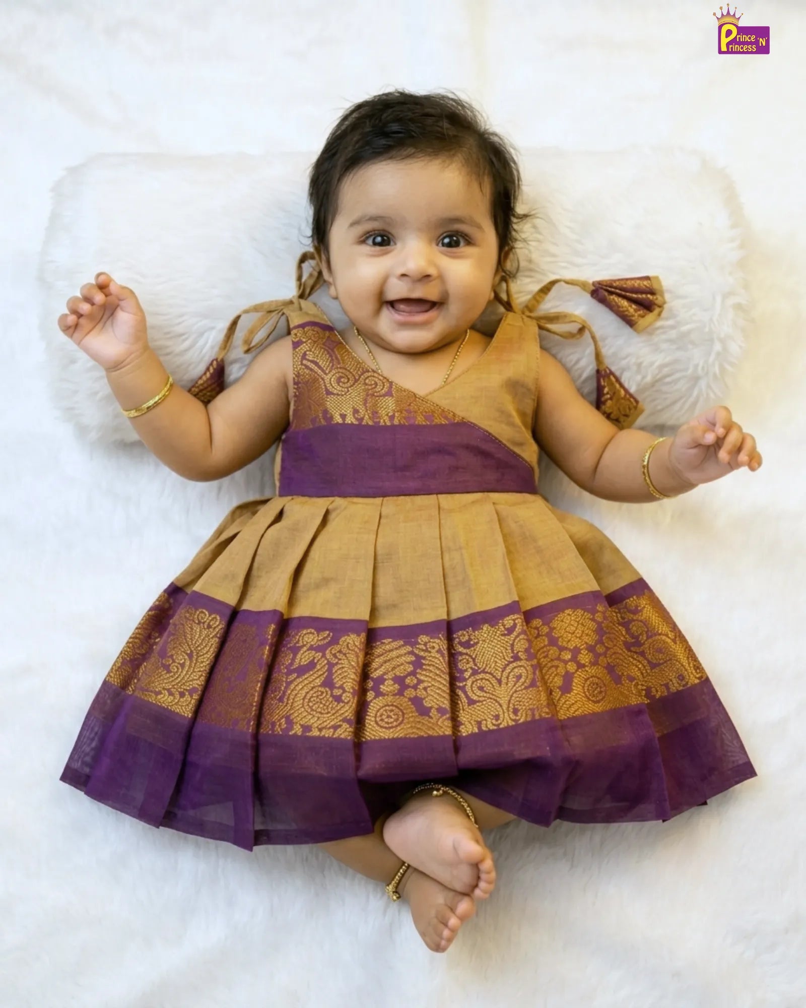 Baby wearing a traditional outfit with purple and gold details on a white background