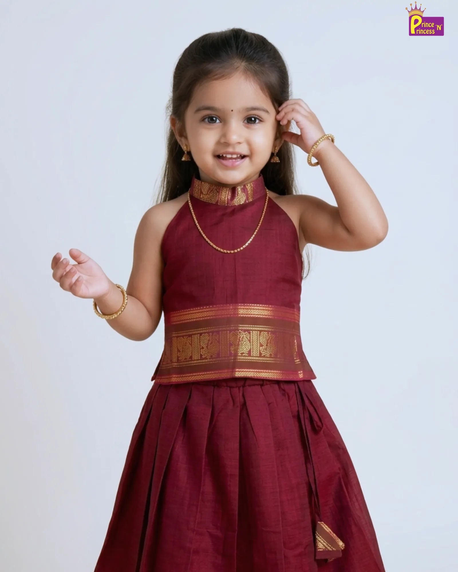 Young girl wearing a maroon traditional dress with gold accents on a white background