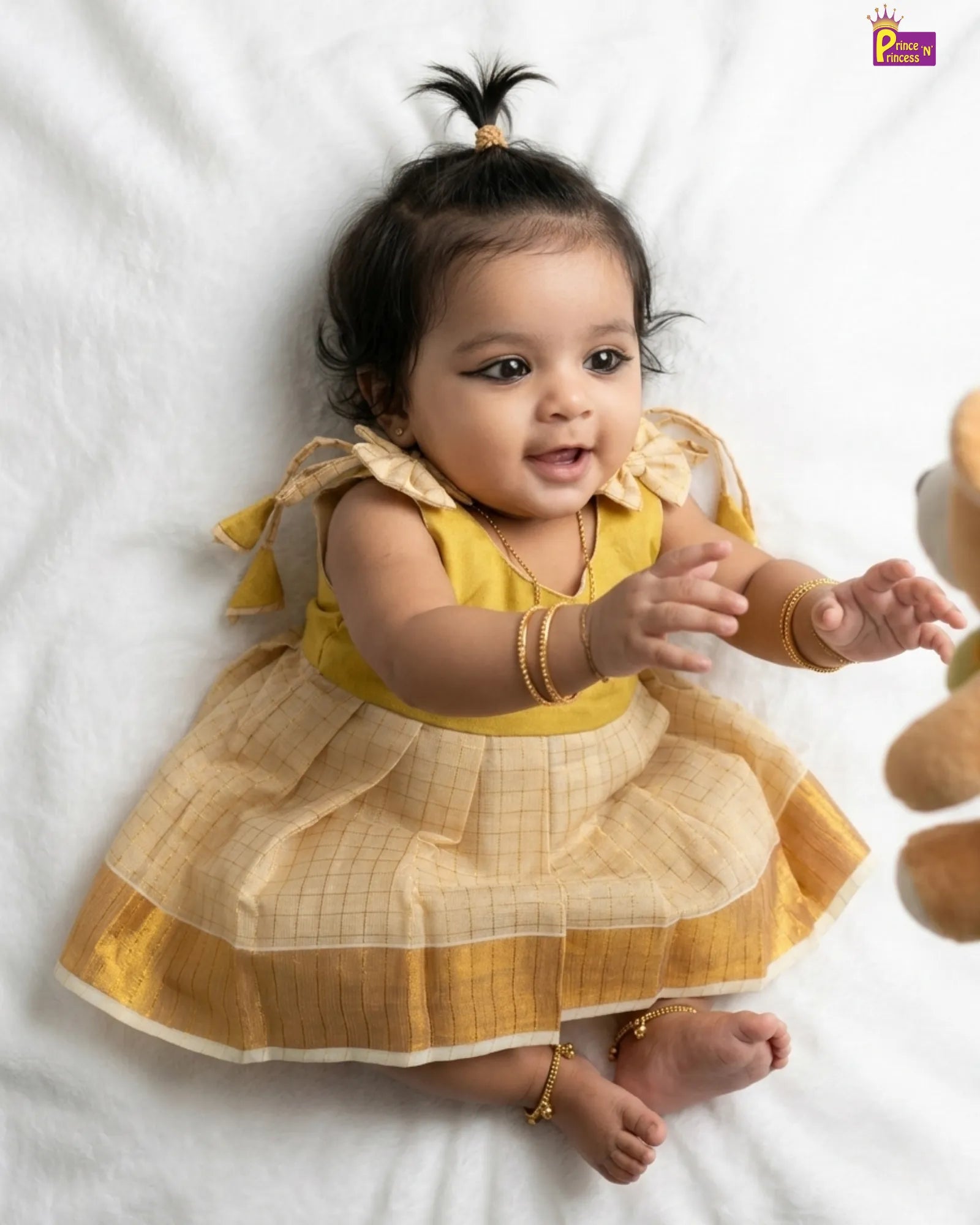 Baby in a yellow dress lying on a white surface
