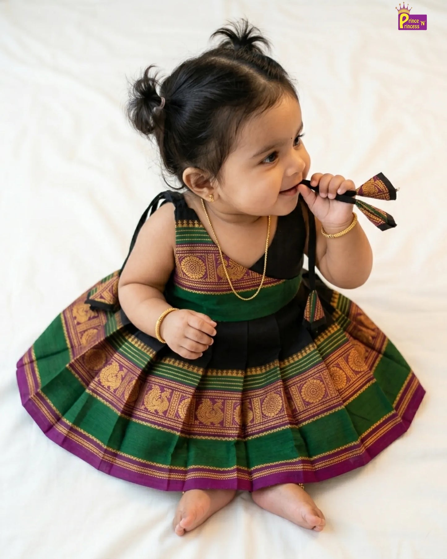 Baby wearing a traditional outfit with green and purple patterns on a white background