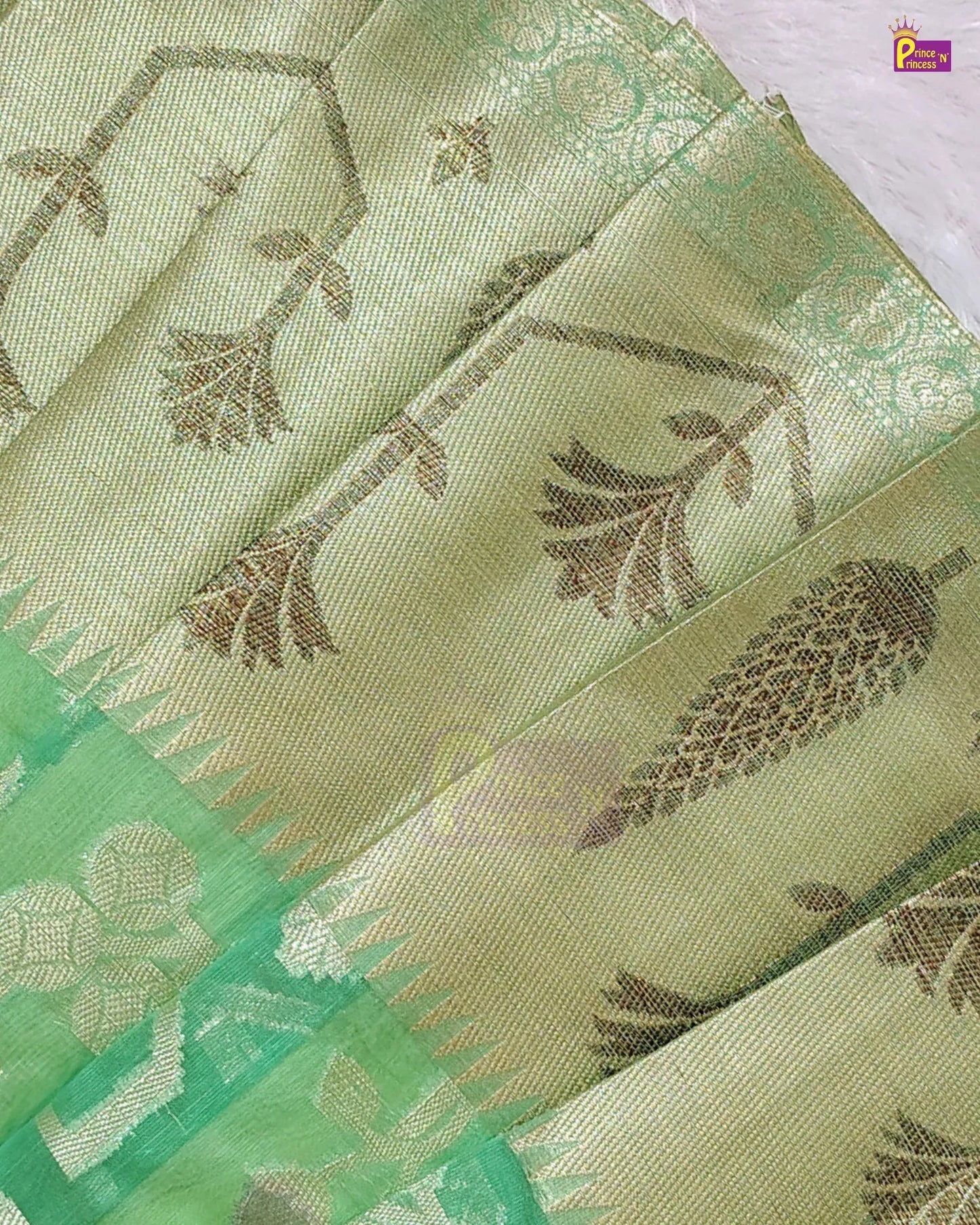 A close-up of a light green silk saree with metallic gold floral motifs and a contrasting green border.