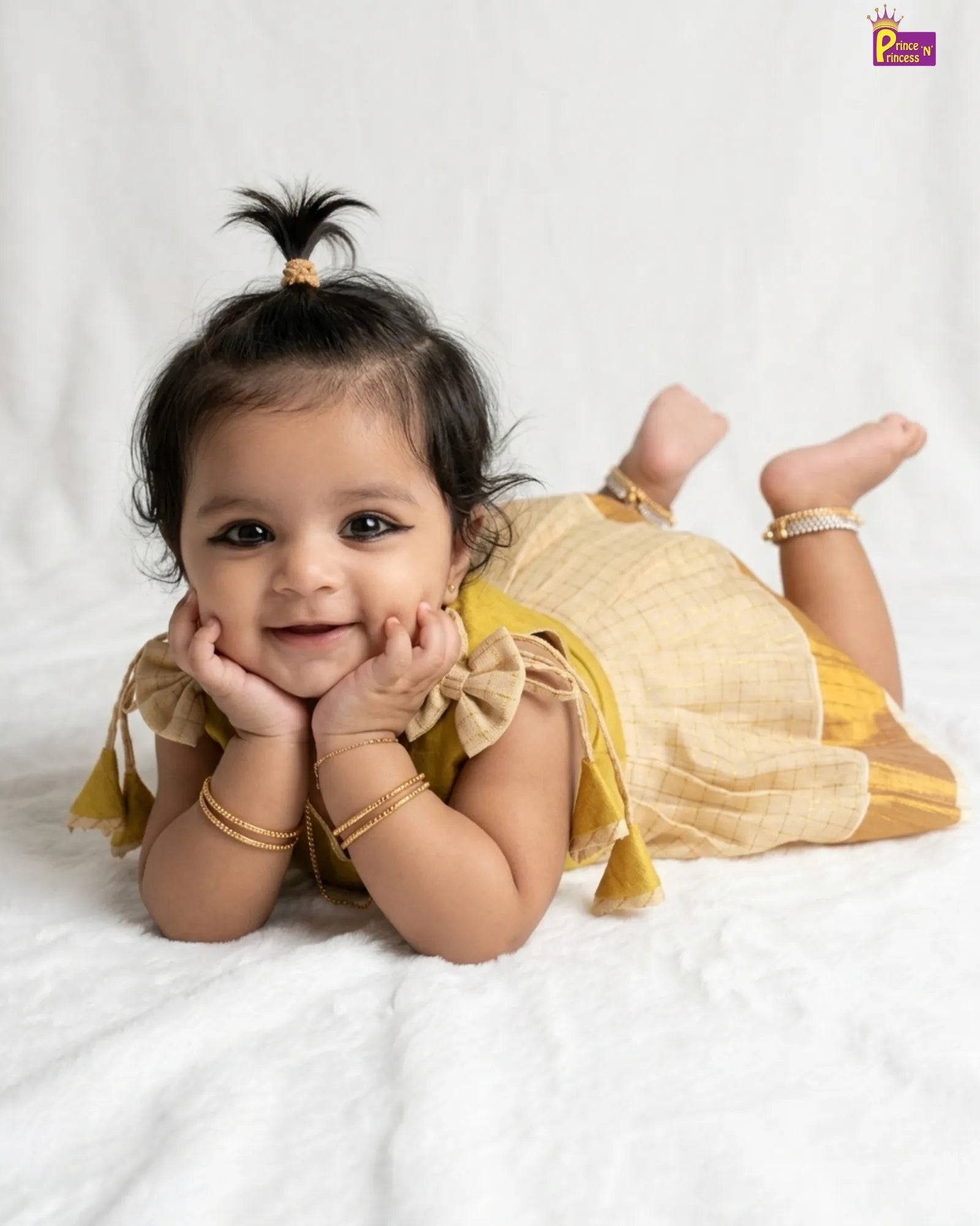 Baby in a yellow outfit lying on a white blanket