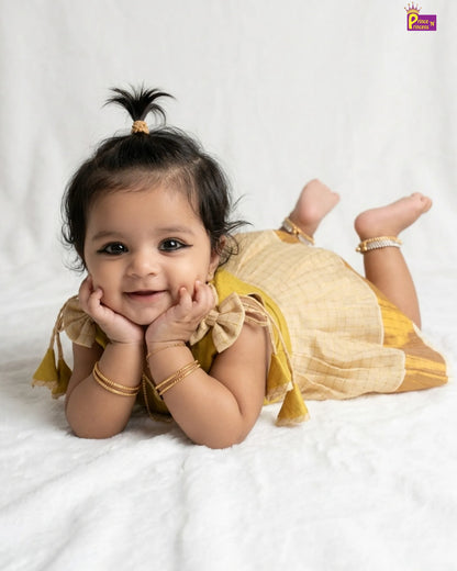 Baby in a yellow outfit lying on a white blanket