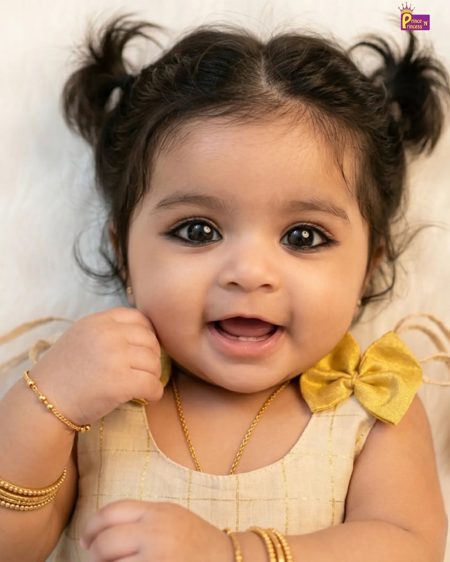 Baby with braided hair, gold jewelry, and a yellow bow
