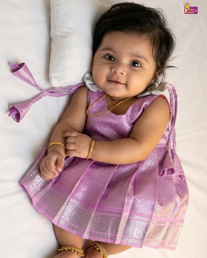 Baby in a pink traditional outfit lying on a white surface