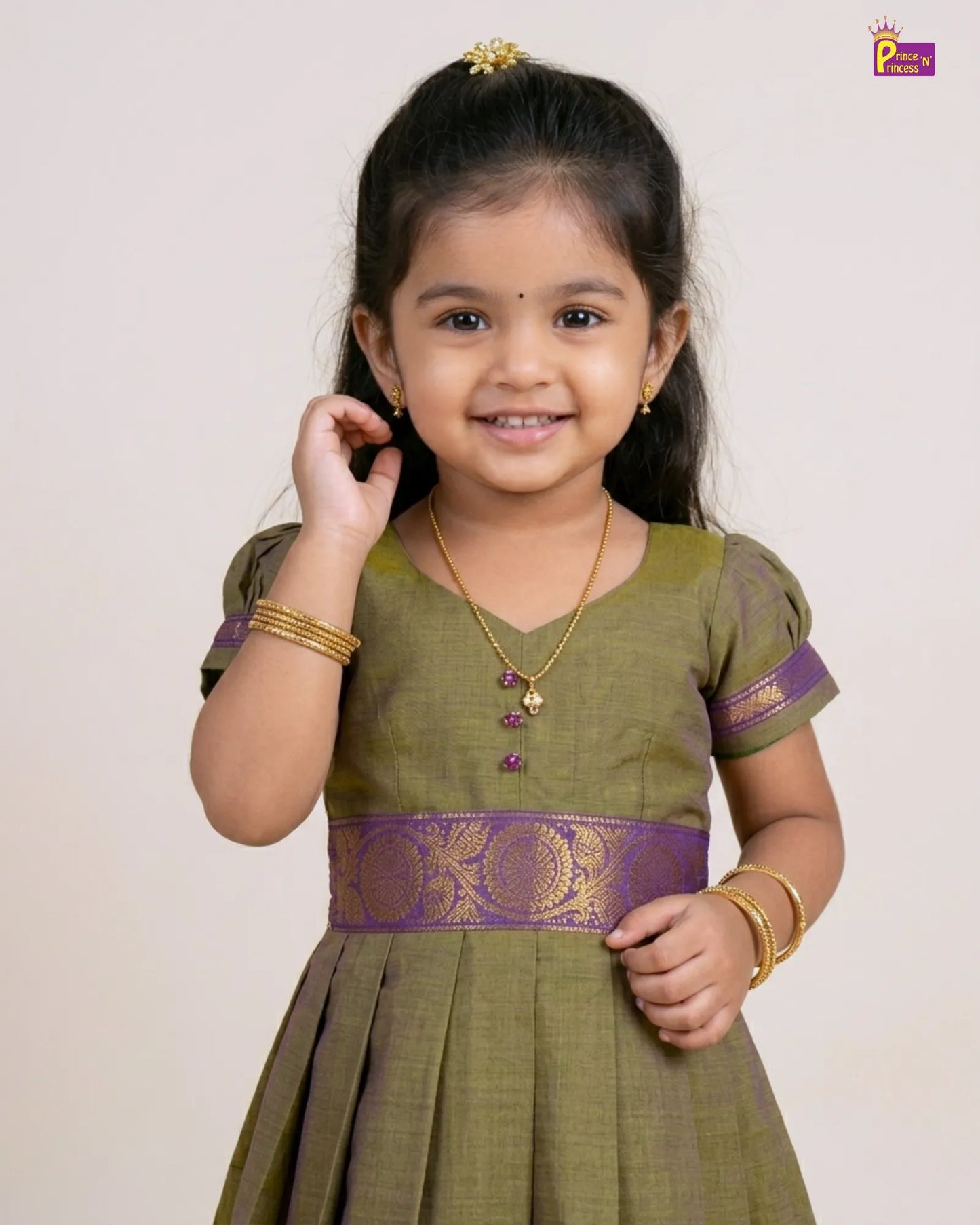 Young girl wearing a green traditional outfit with purple accents on a plain background