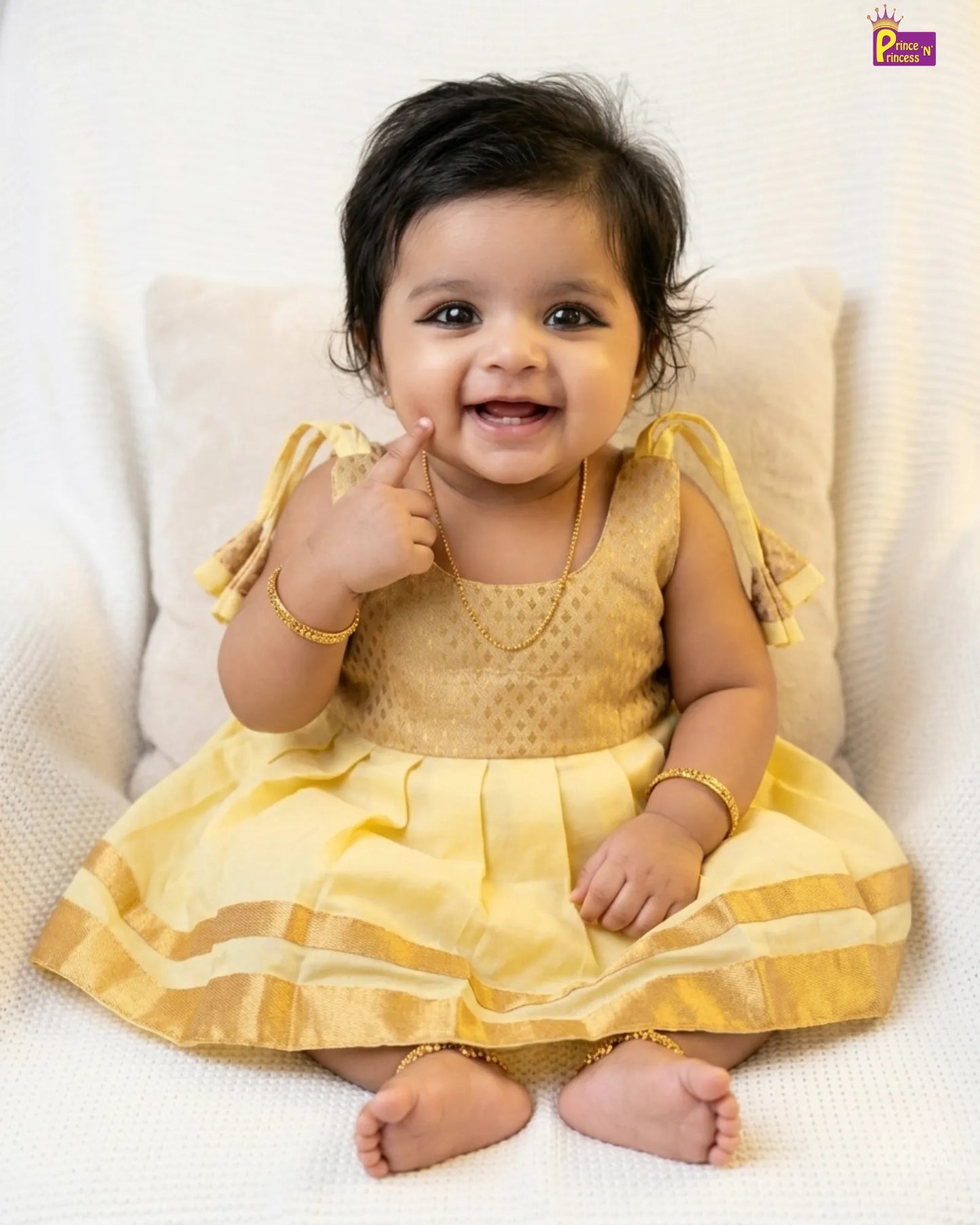 Baby in a yellow dress sitting on a white surface