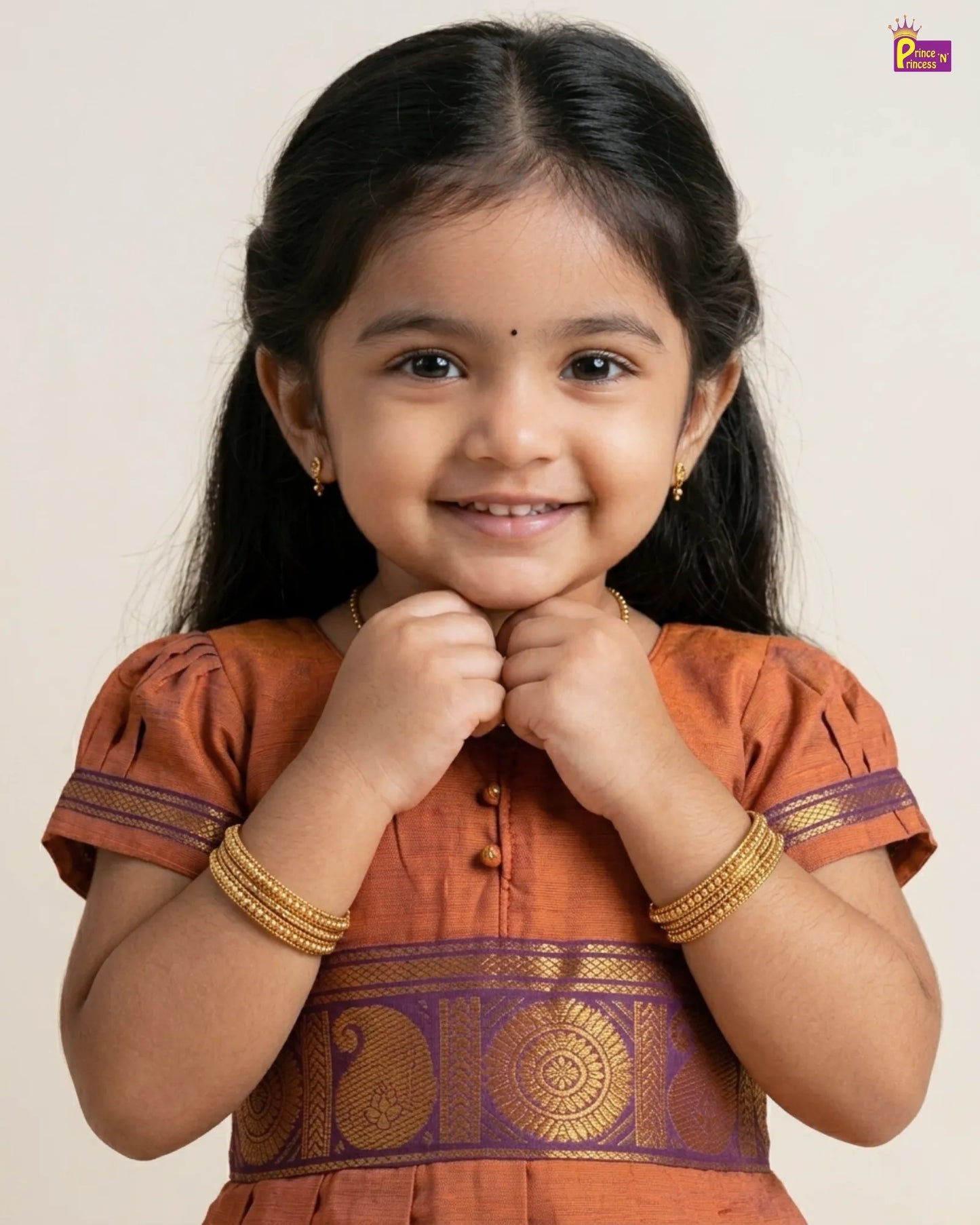 Young girl in an orange traditional outfit with gold jewelry on a plain background