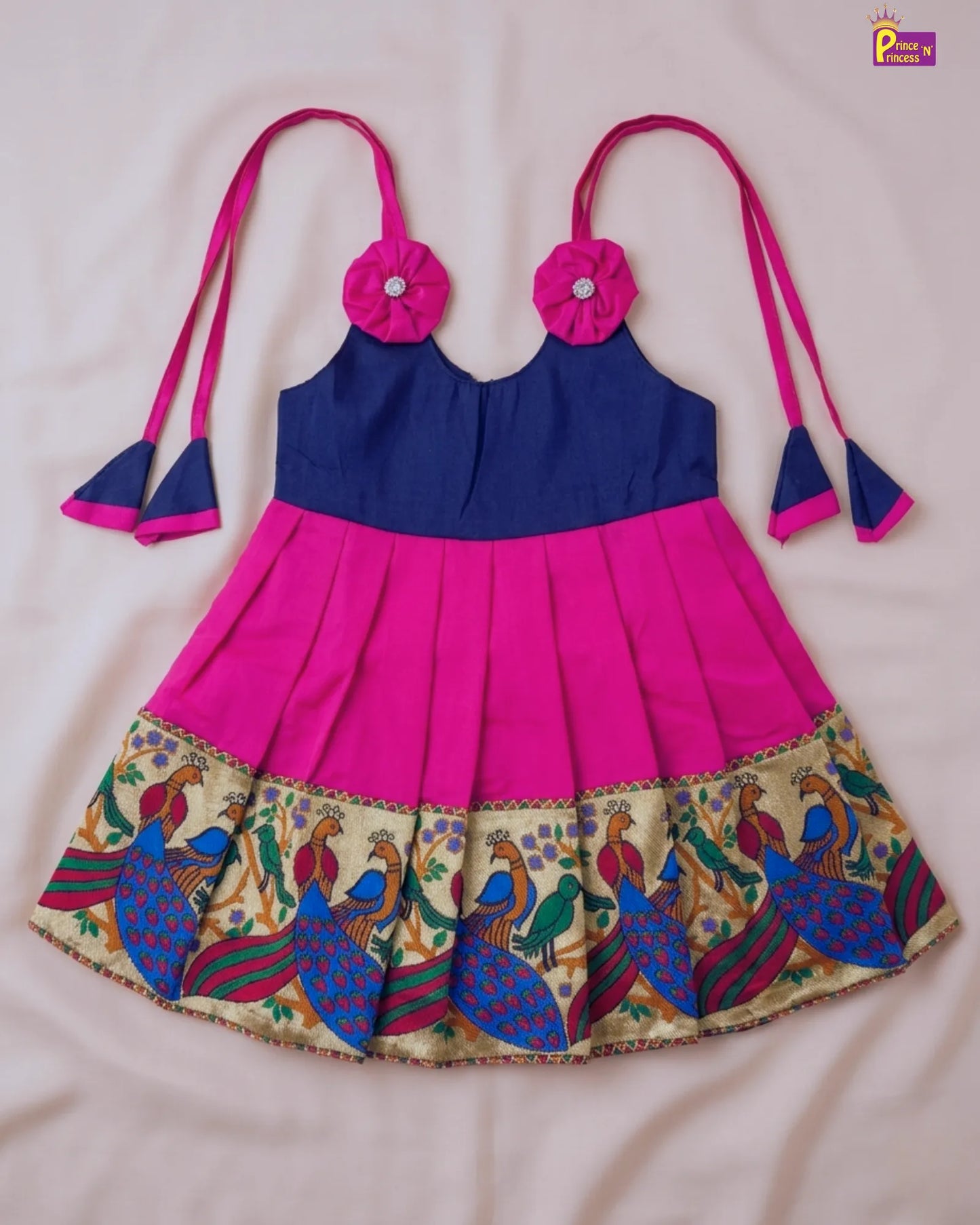 Children's outfit with pink and blue top and skirt featuring peacock patterns on a light background.