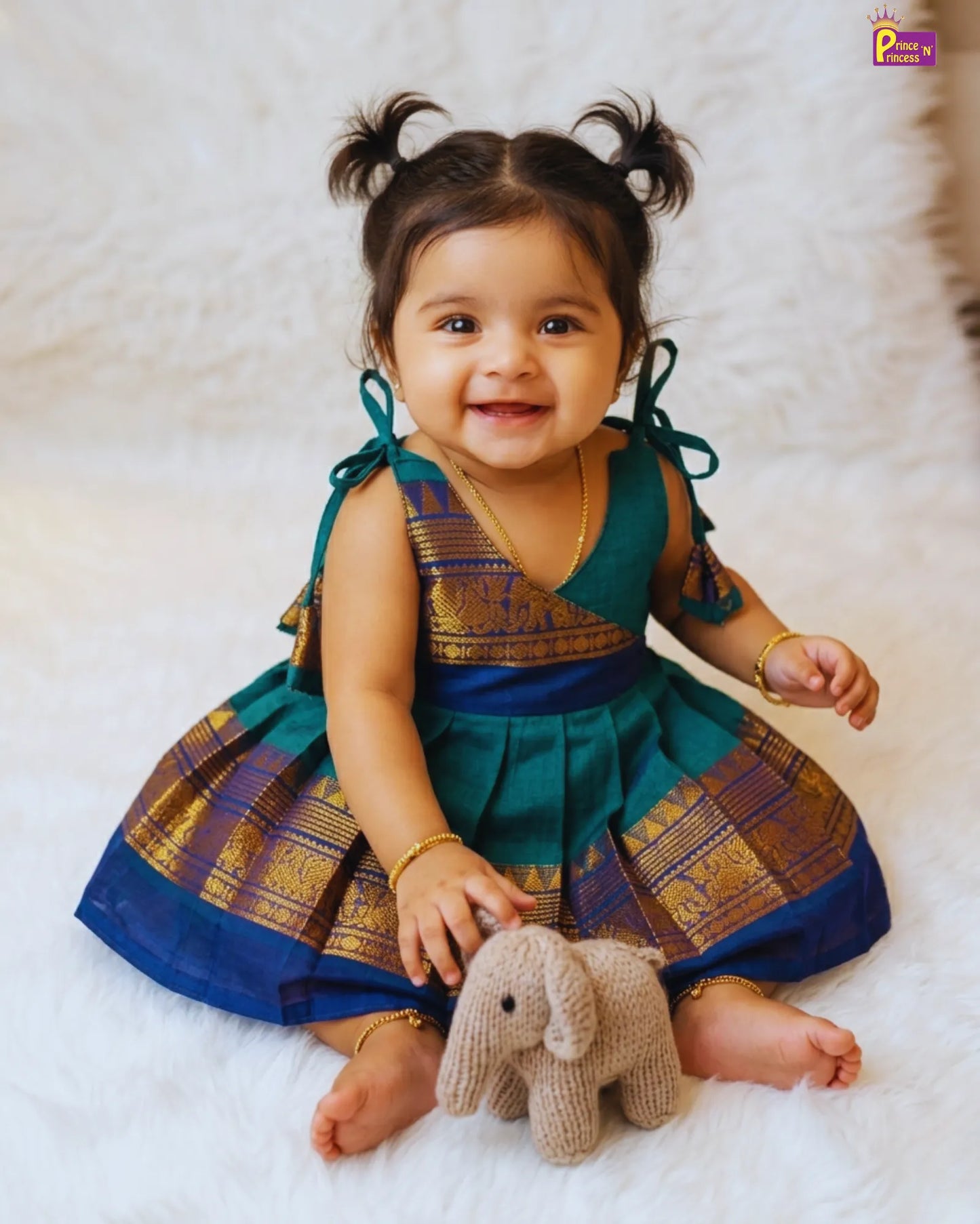 Child in a traditional outfit holding a toy elephant on a white background