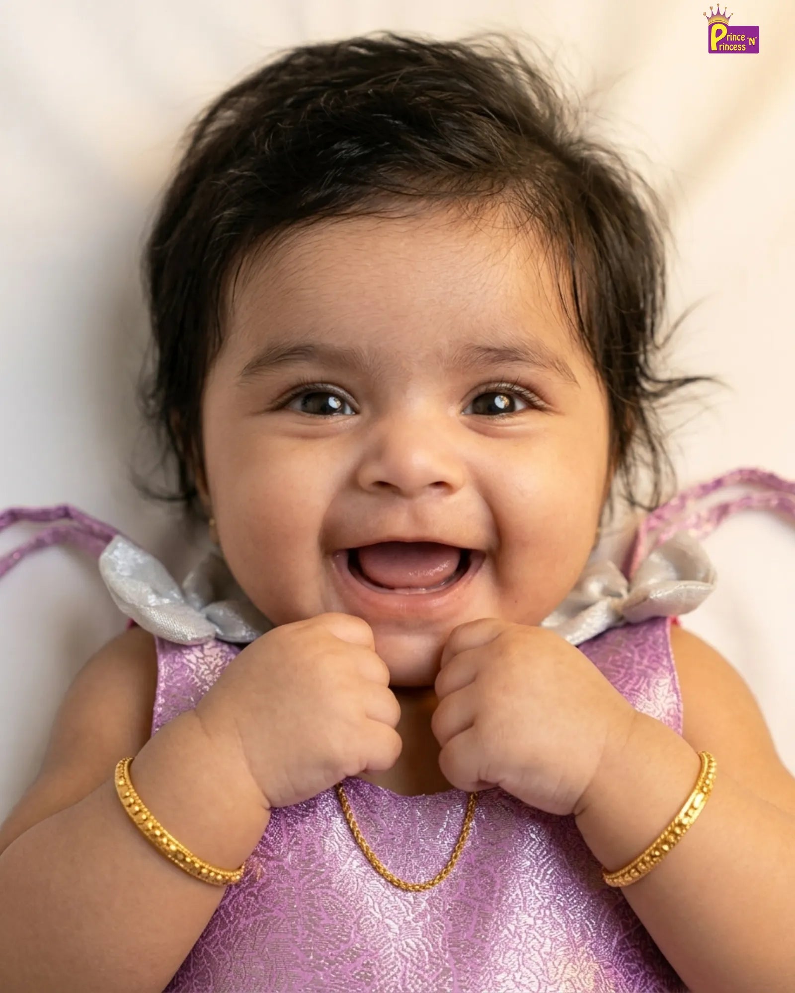 Baby in a purple dress with gold jewelry on a light background