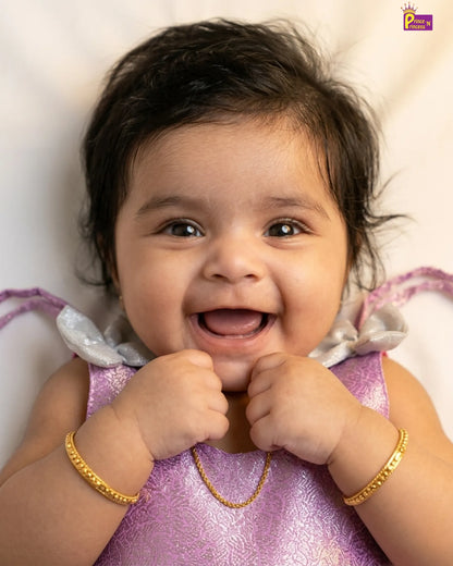 Baby in a purple dress with gold jewelry on a light background