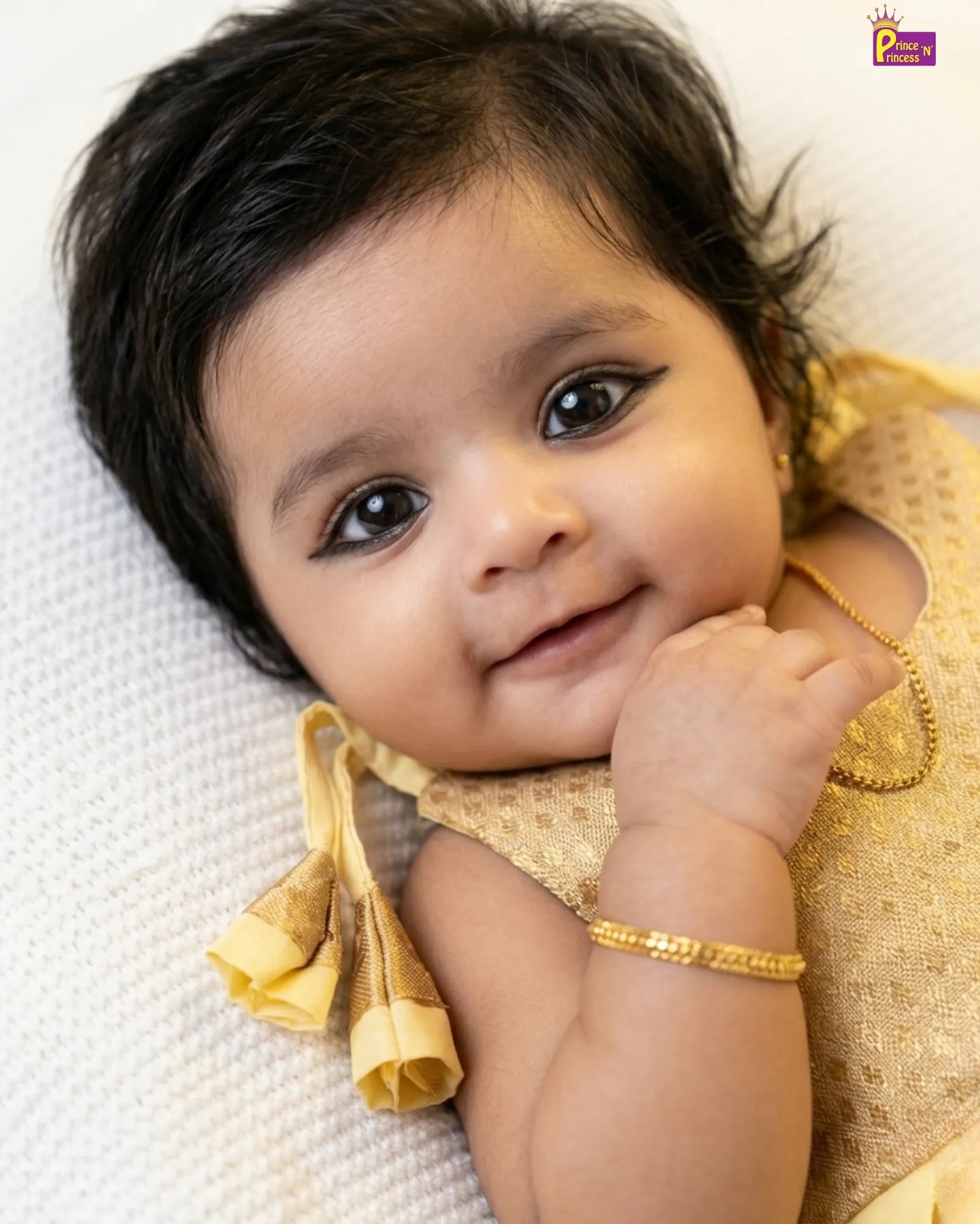 Baby in a gold outfit lying on a white blanket