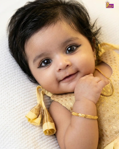 Baby in a gold outfit lying on a white blanket