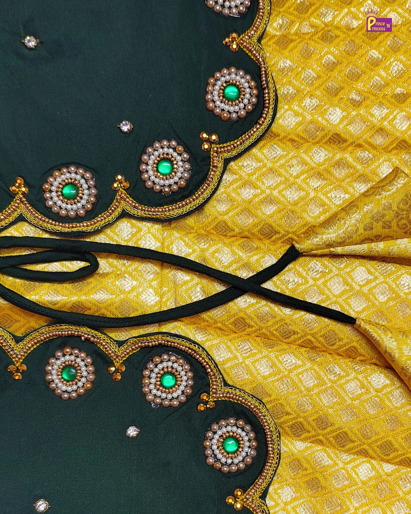 Close-up of a yellow fabric with green gemstone and pearl embellishments on a black border.