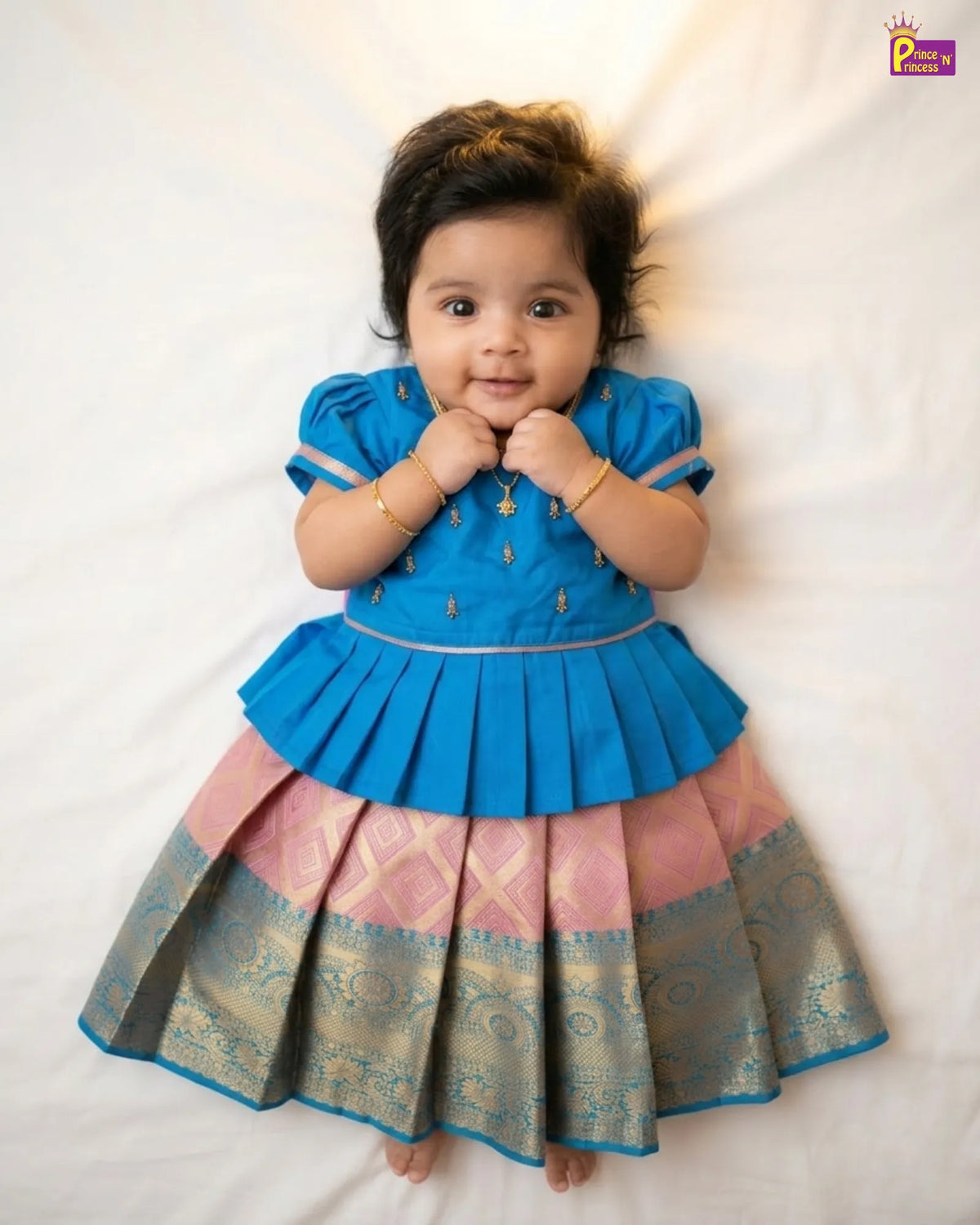 Baby wearing a blue and pink traditional outfit on a white background
