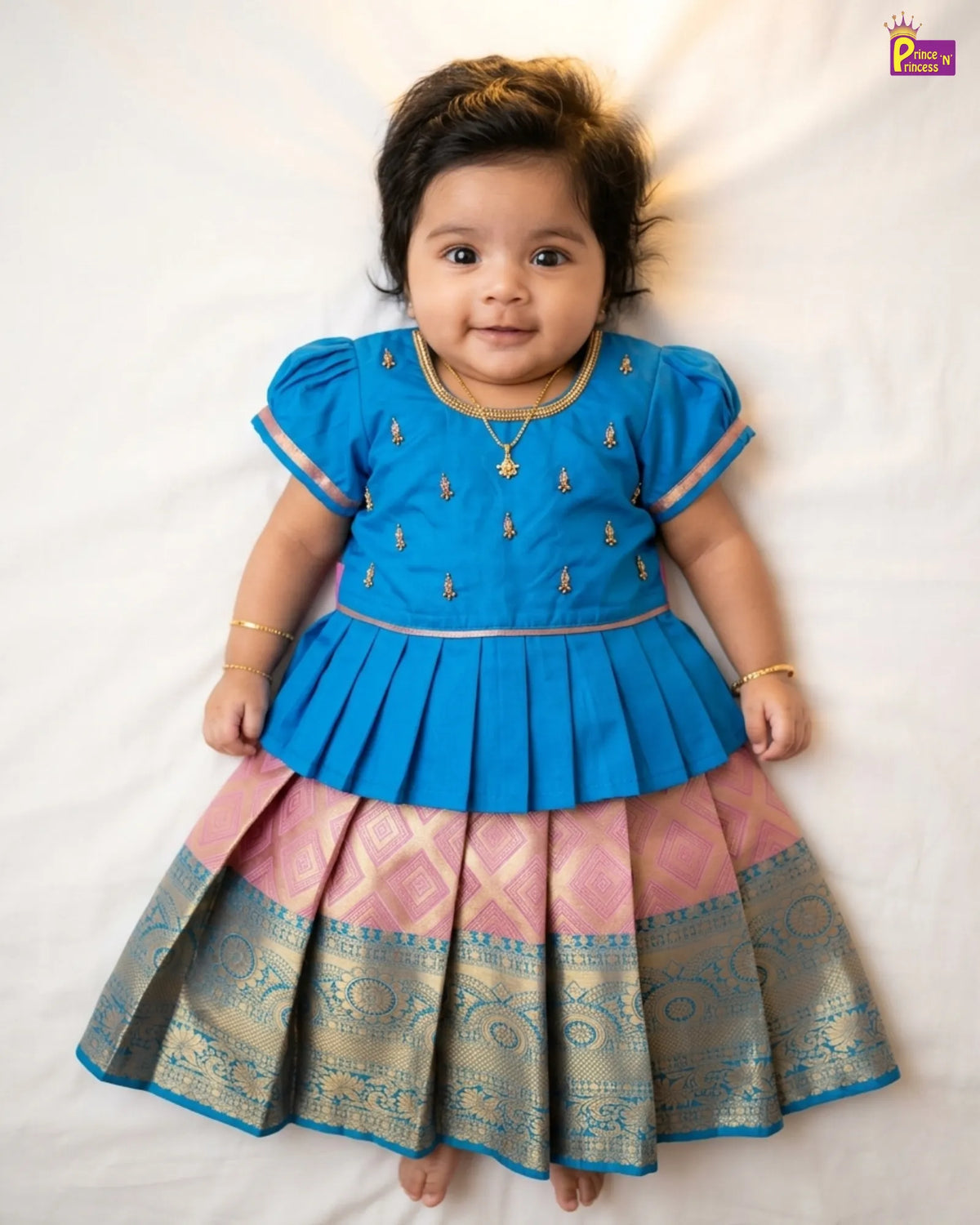 Baby wearing a blue and pink traditional outfit on a white background