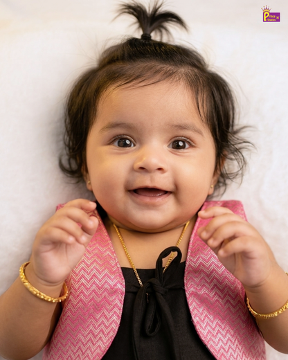 Baby wearing a pink jacket over a black outfit with gold jewelry on a white background