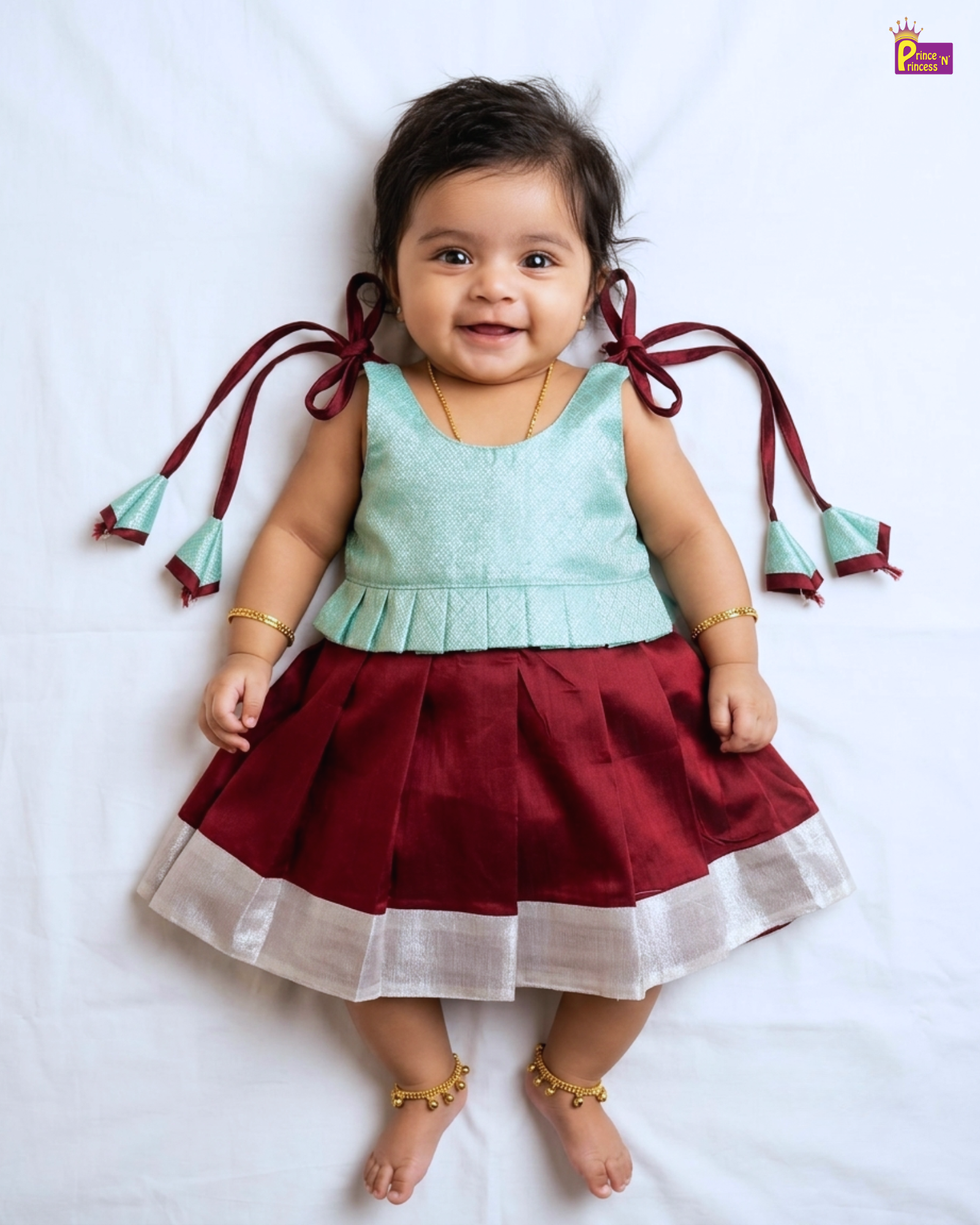 Baby wearing a light blue top and red skirt with tassels on a white background