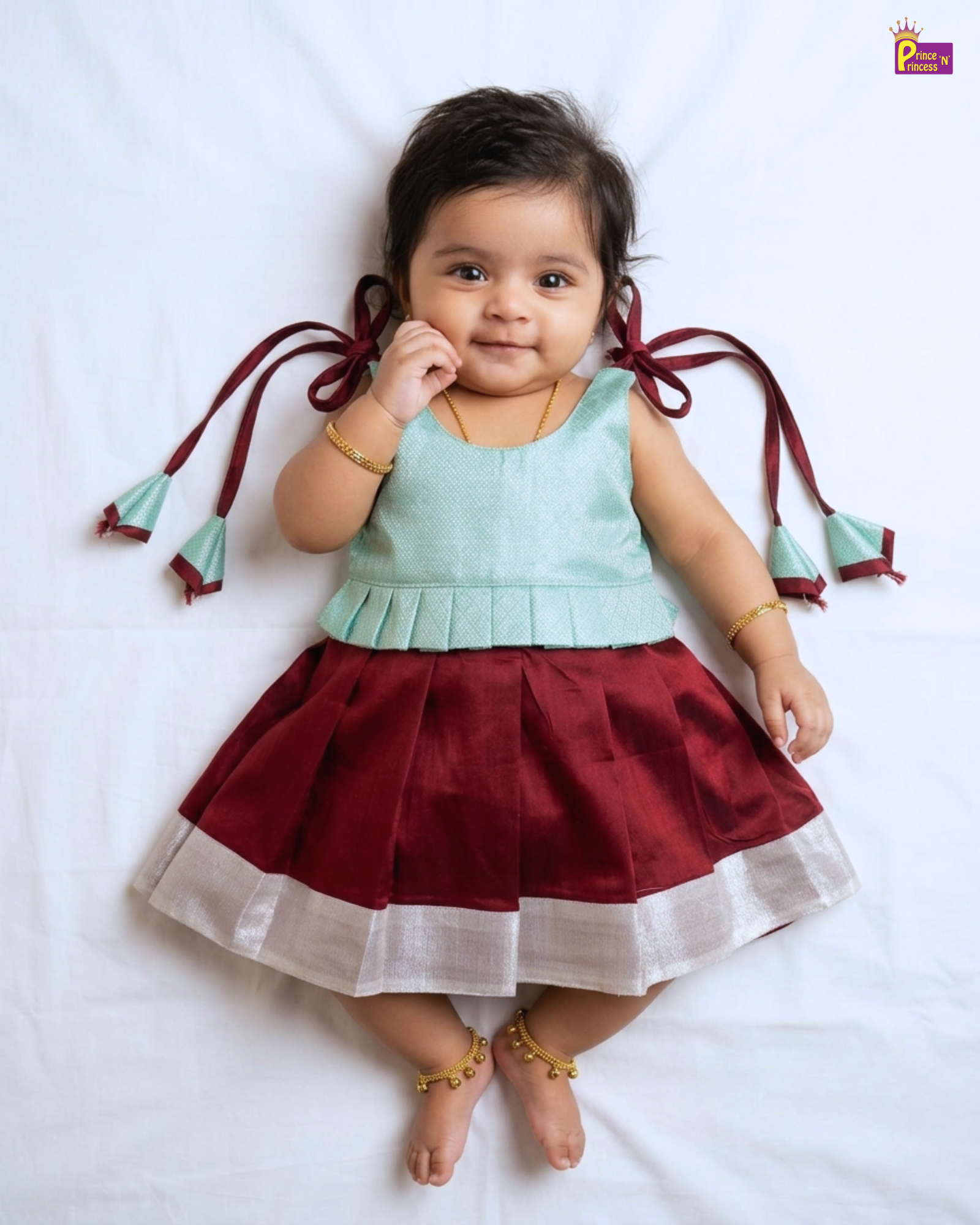 Baby wearing a light green top and red skirt with white trim on a white background